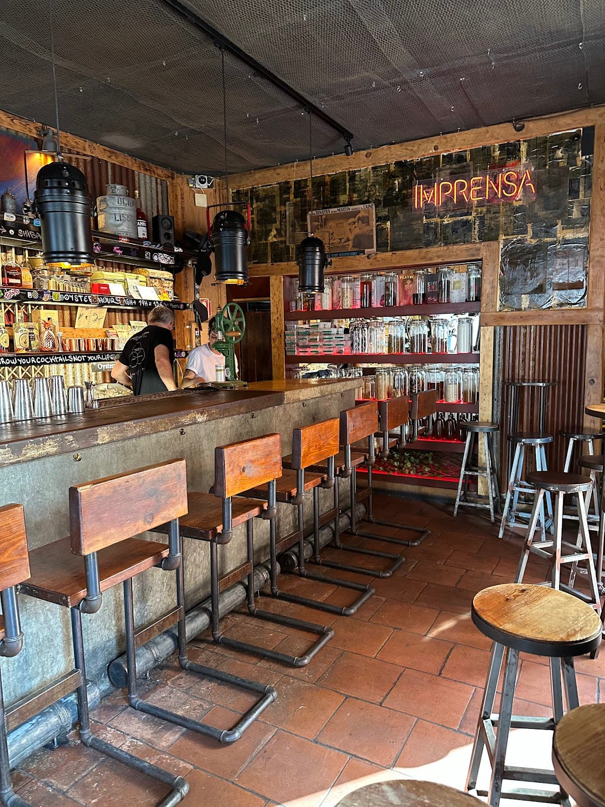 Rustic bar area with wooden stools and neon sign reading Imprensa in Lisboa