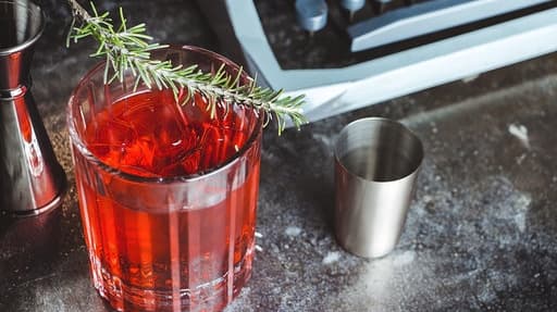 Close-up of a red cocktail with rosemary garnish on a bar counter in Lisboa