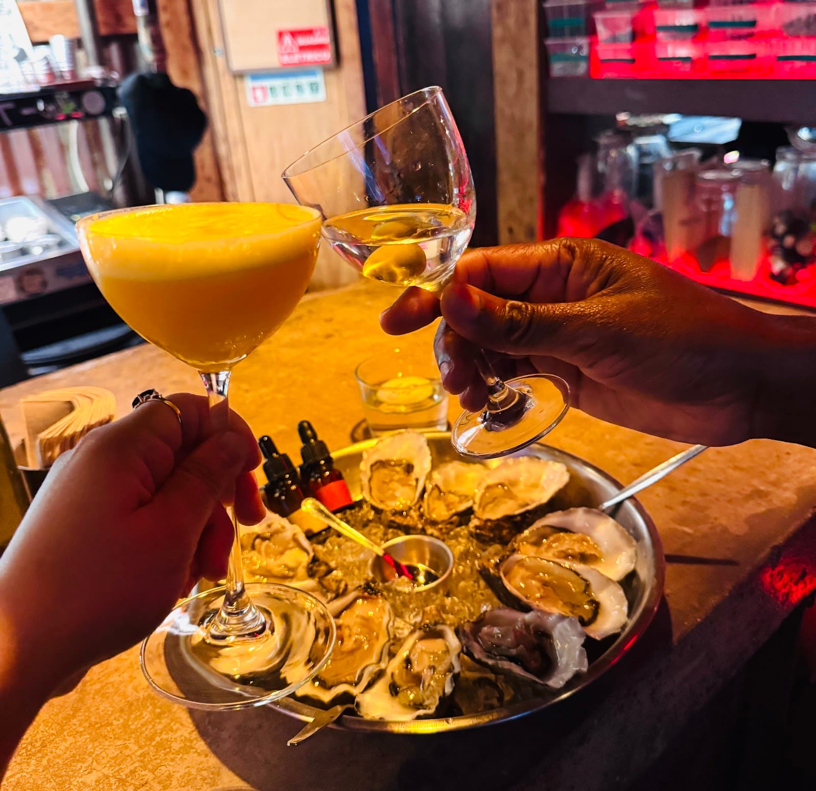 Cocktail glasses raised over a tray of oysters on a bar counter in Lisboa