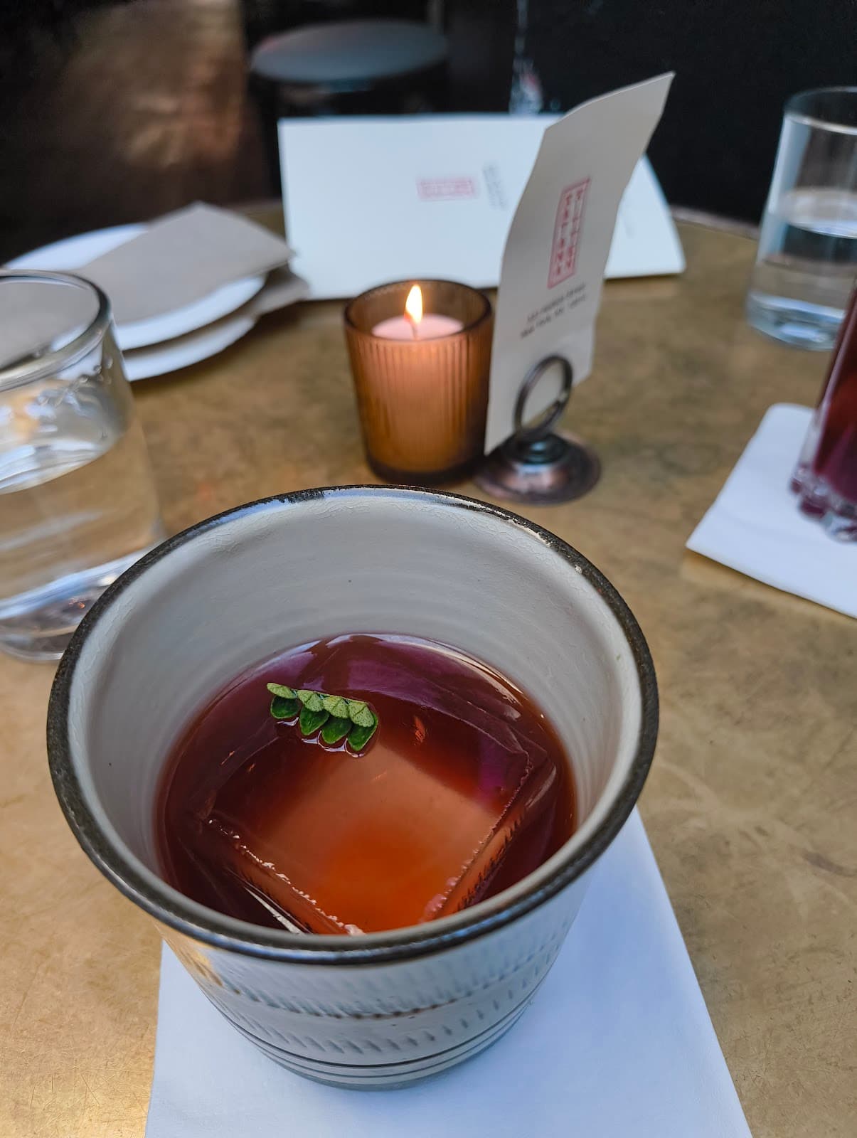 Elegant cocktail with large ice cube and garnish on a table with candle in New York