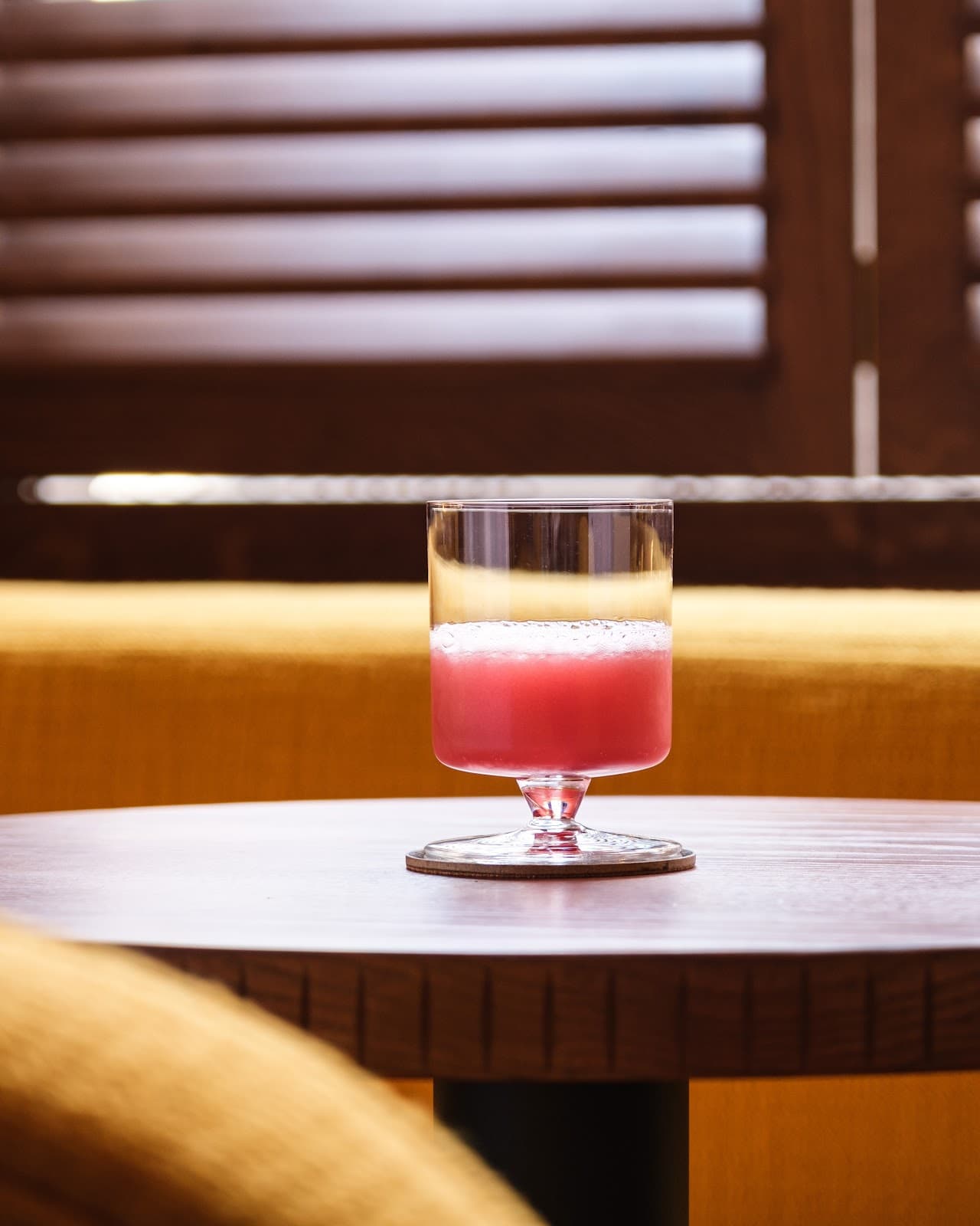 Pink cocktail in glass on wooden table with warm lighting in London