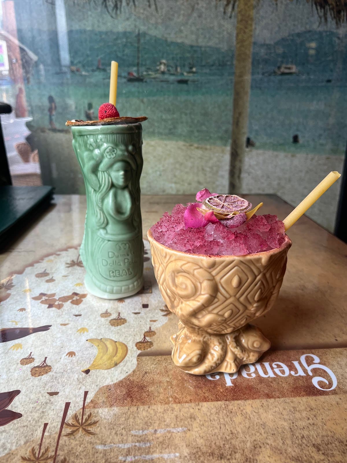 Two creative cocktails on a table with a beach mural in the background in London