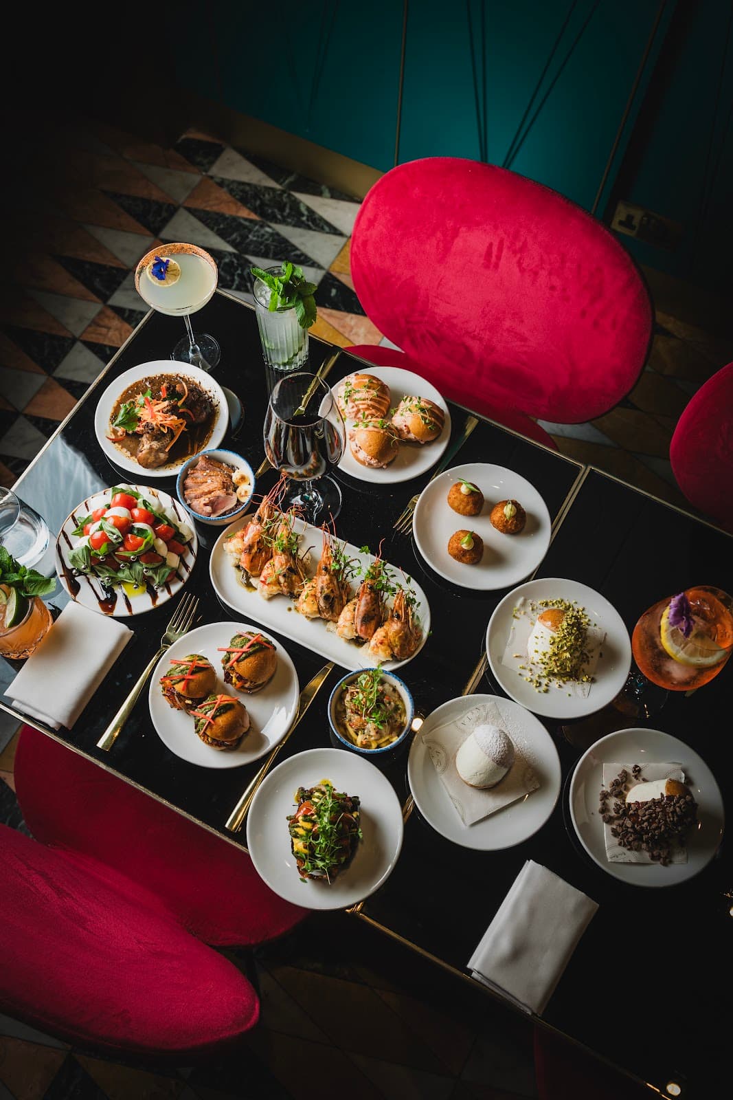 Assorted elegant dishes and cocktails on a table with red chairs in London