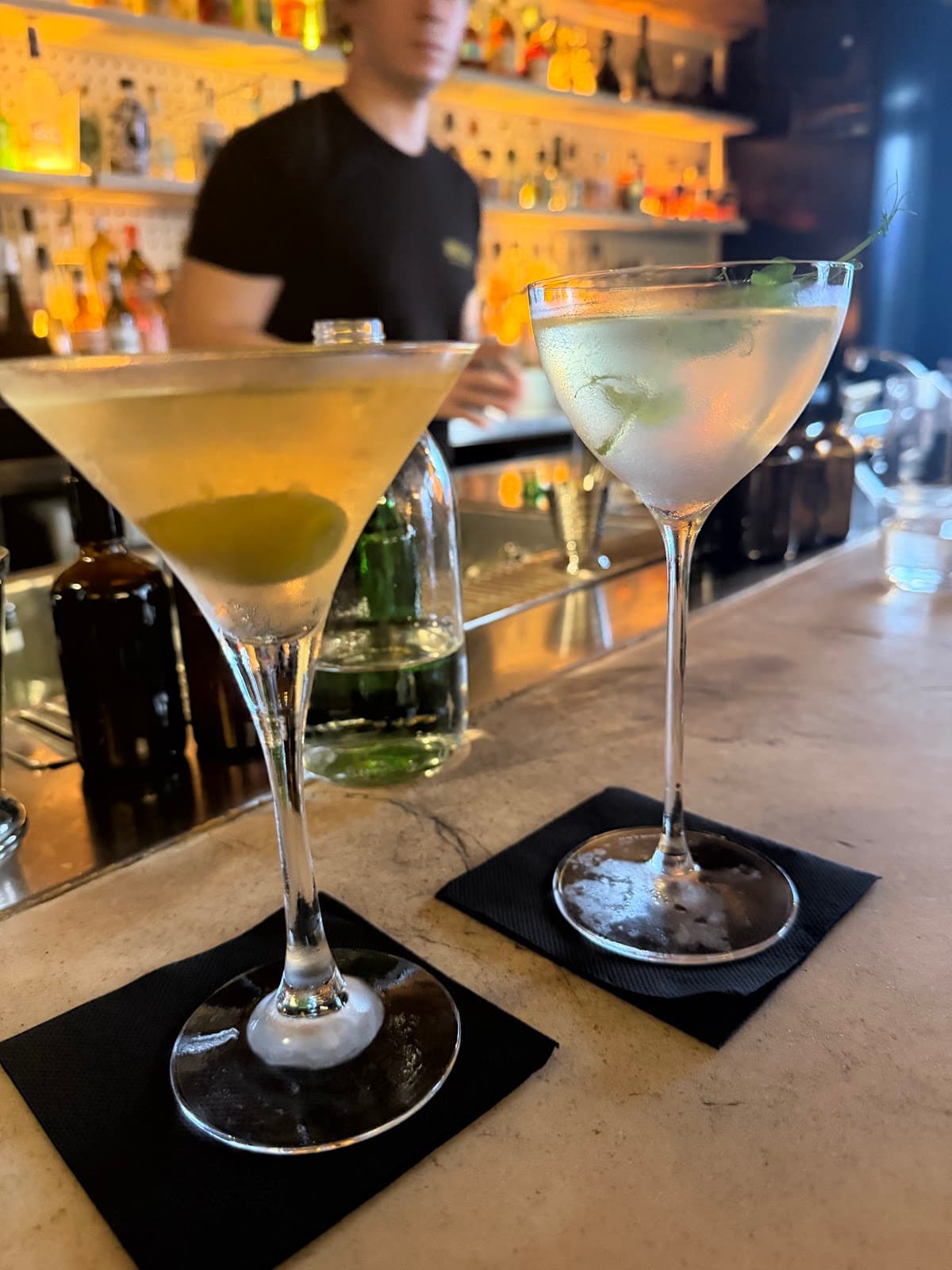 Two cocktails on a bar with a blurred bartender in the background in Paris
