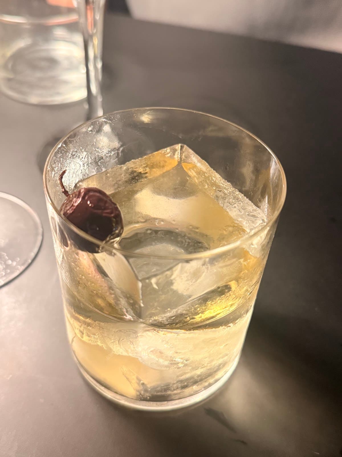 Close-up of a cocktail with a large ice cube and cherry garnish in Paris