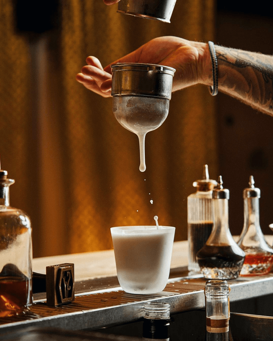 Close-up of cocktail preparation with a milk froth strainer at a bar