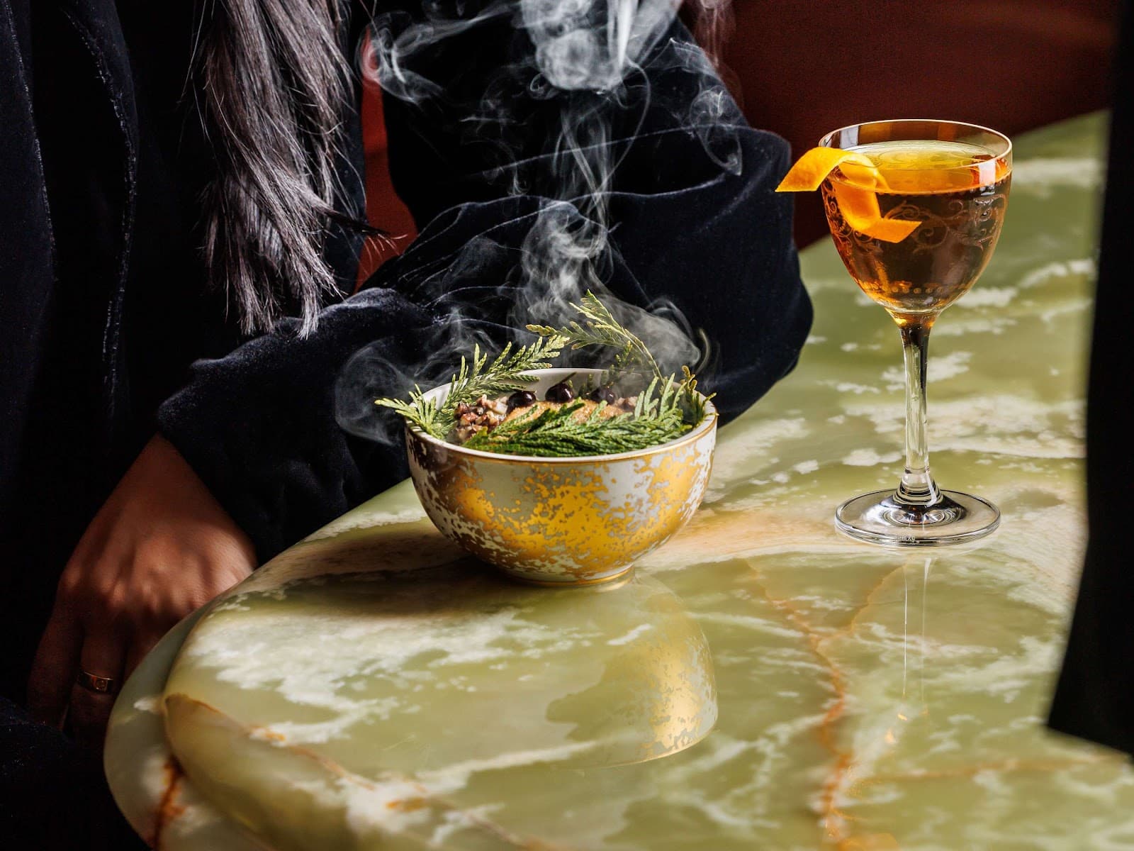 Elegant cocktail with orange twist on marble table with smoking herbs in Toronto