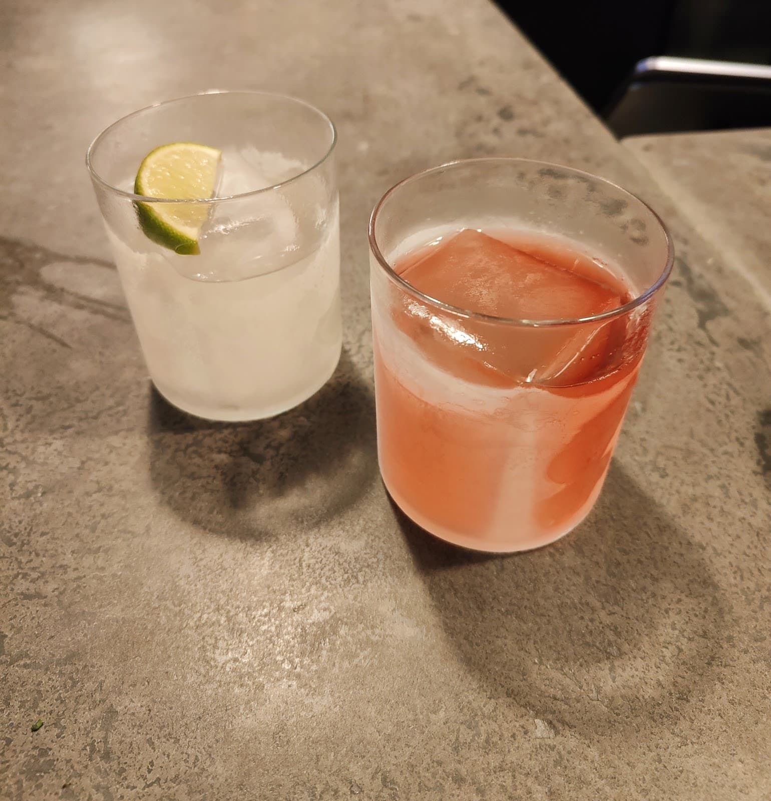 Two cocktails on a concrete counter, one with lime wedge in London
