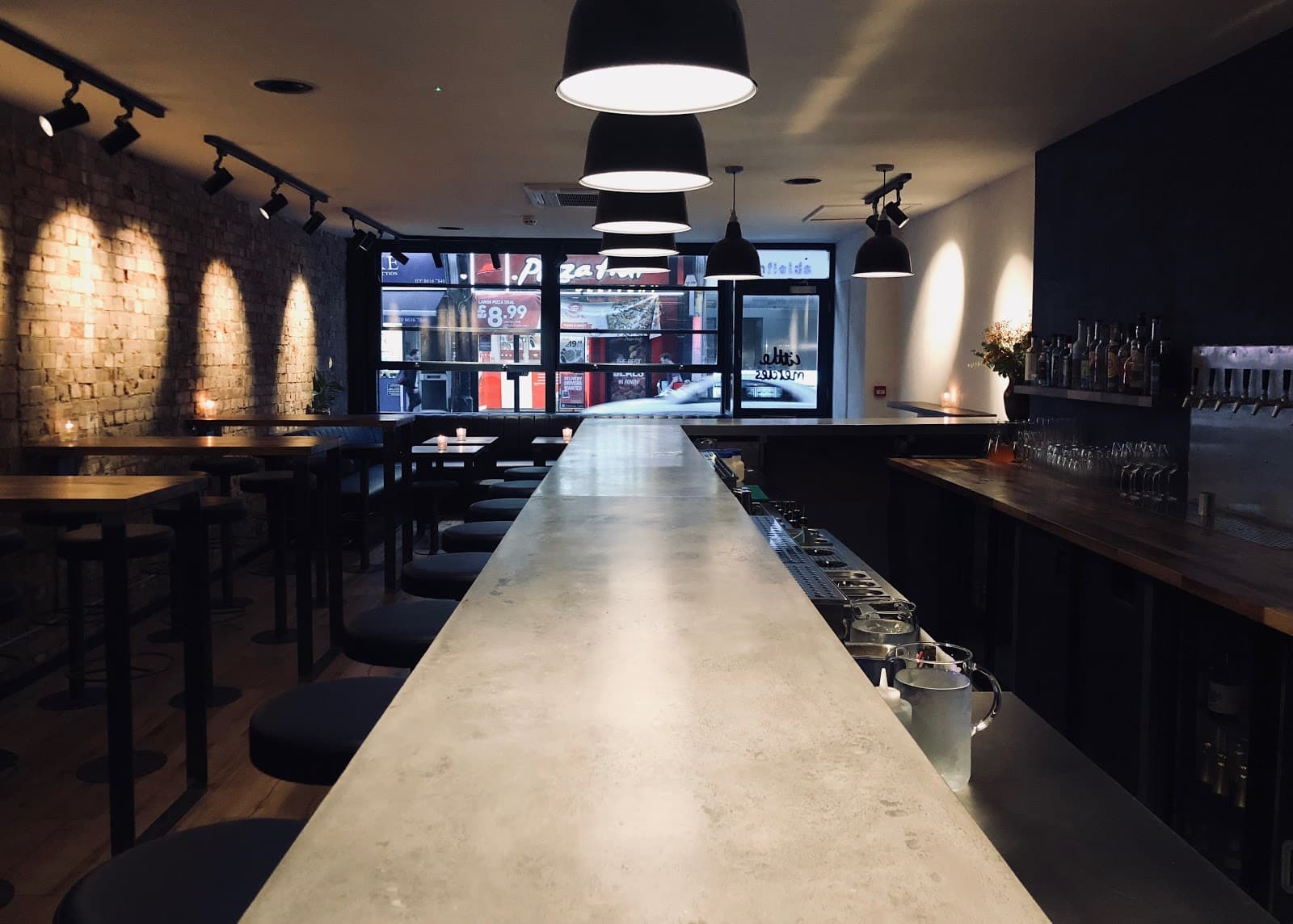 Modern bar interior with concrete counter and exposed brick wall.