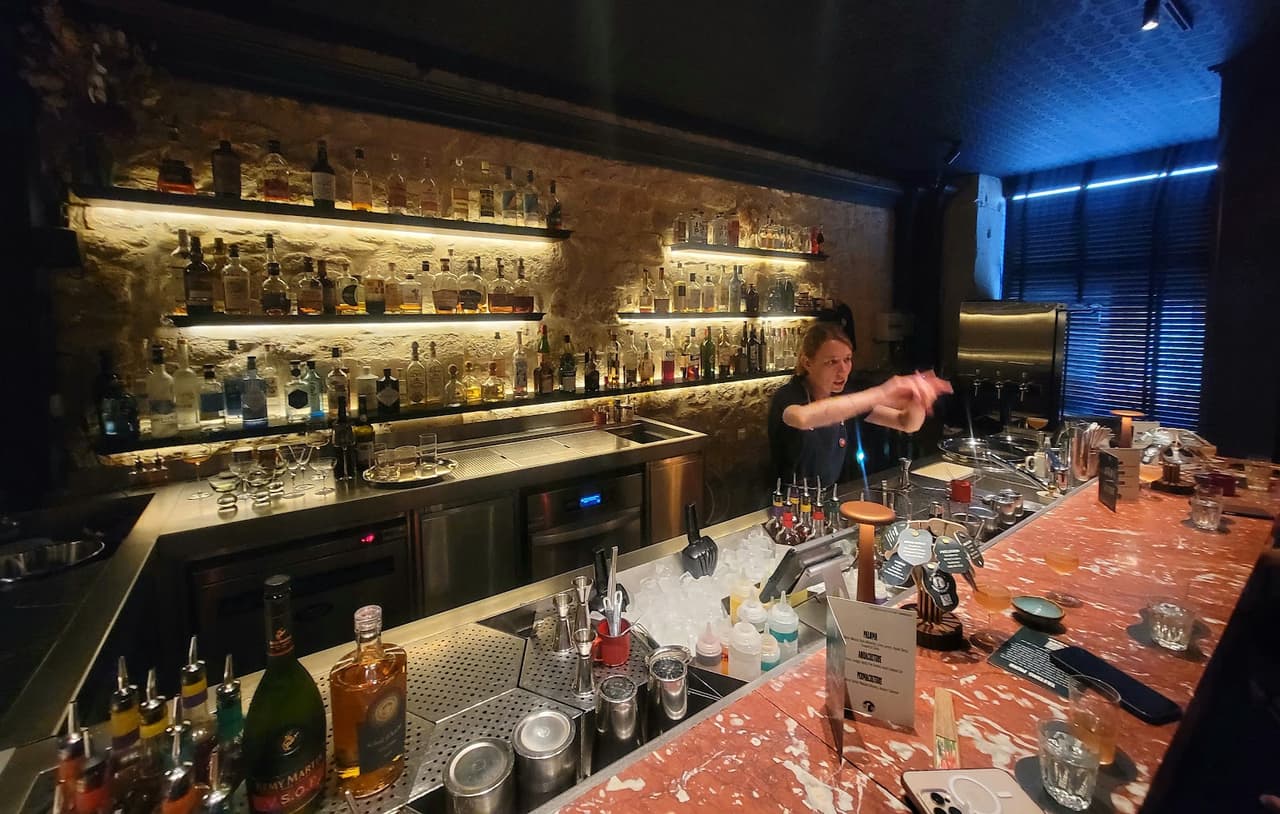 Bar counter with bottles and bartender in a dimly lit setting in Paris