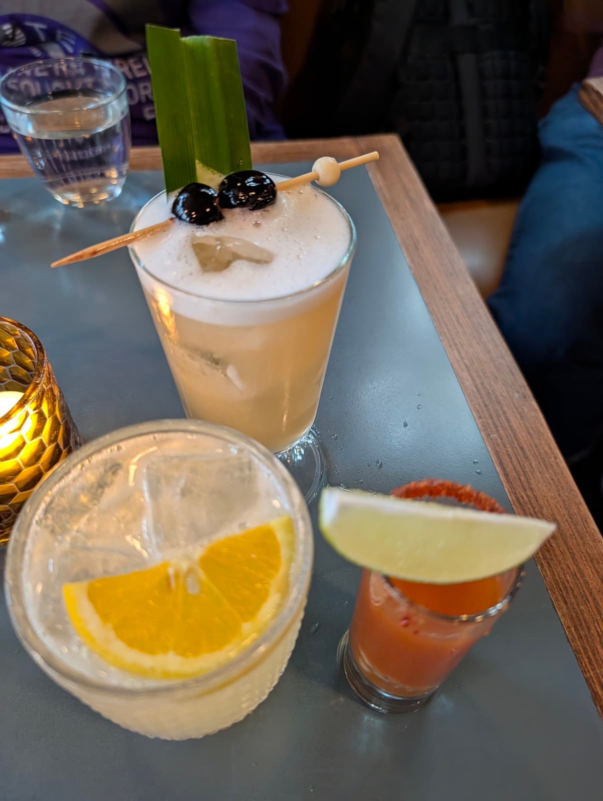 Three cocktails on a table with garnish and a lit votive candle in San Francisco