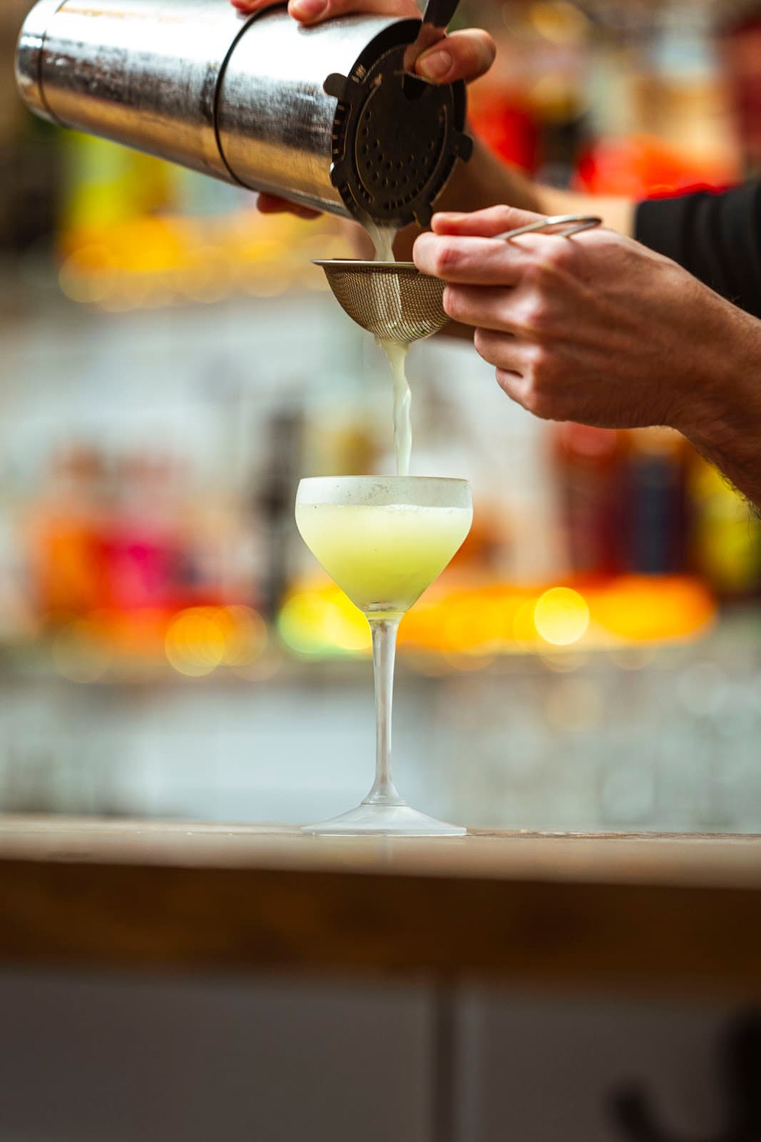 Bartender straining a yellow cocktail into a glass in Edinburgh