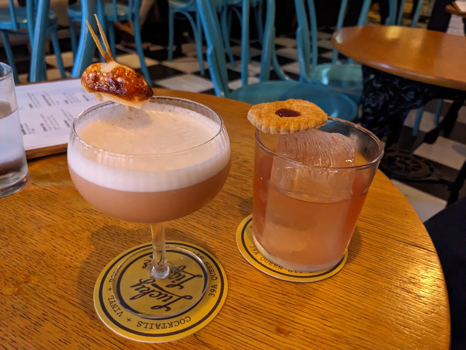Two cocktails on a wooden table with garnishes in a bar setting in Edinburgh