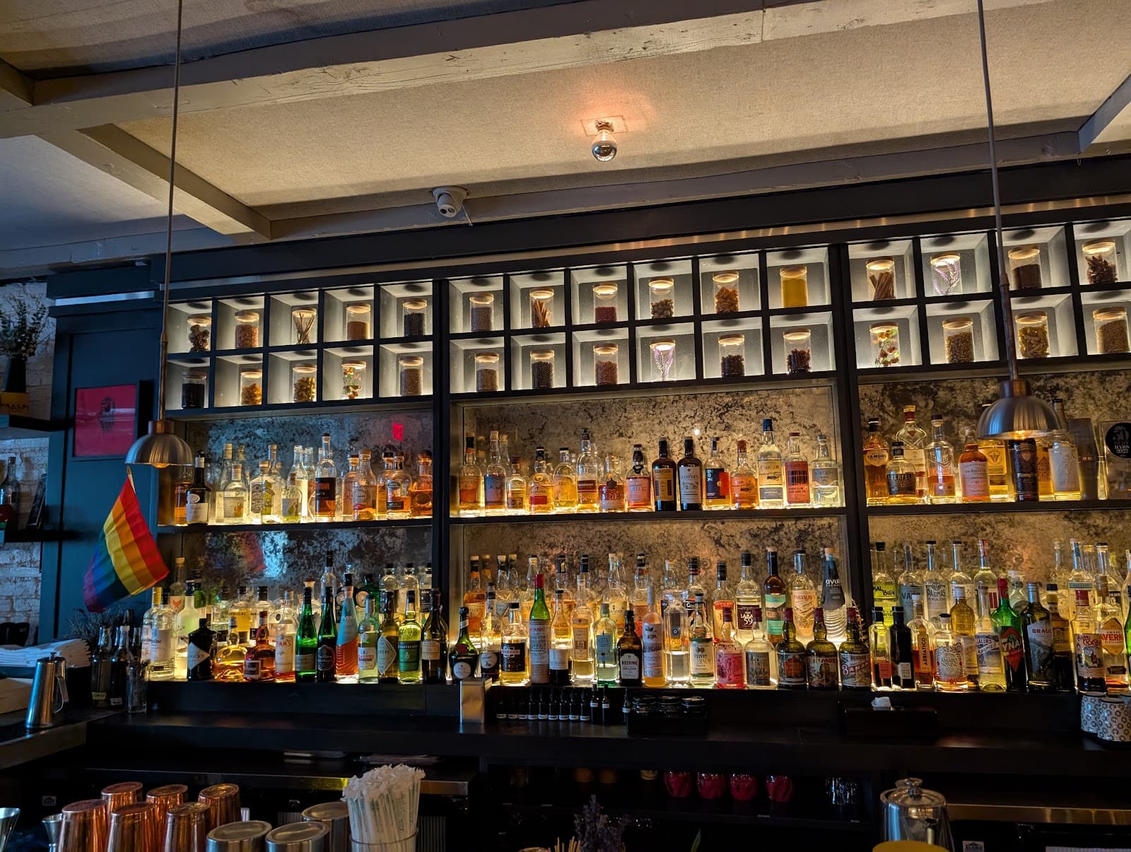 Well-lit bar with a variety of bottles and a rainbow flag in New York