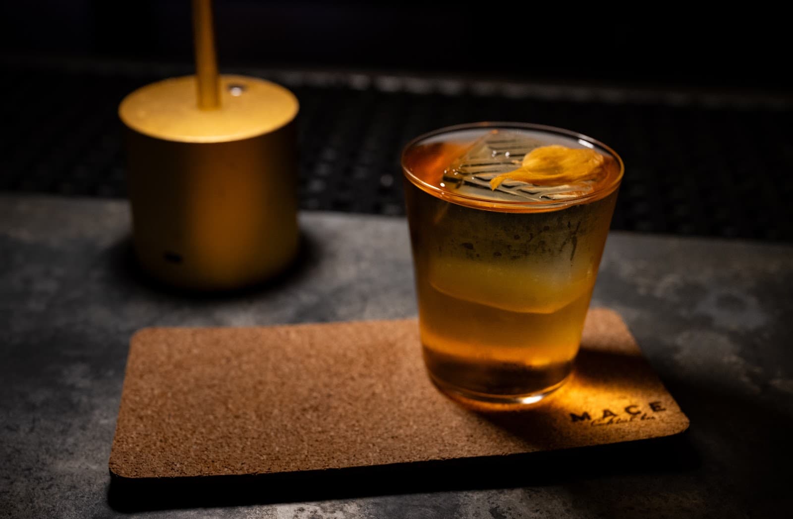 Cocktail in a glass with garnish on a cork mat, dimly lit. in New York