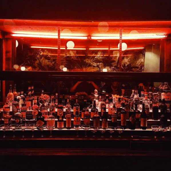 Dimly lit bar counter with various bottles and red lighting