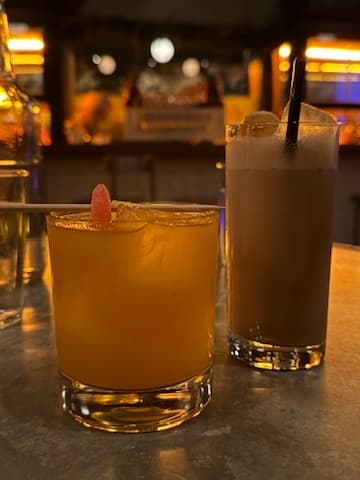 Two cocktails on a bar counter with dim lighting in the background in Toronto