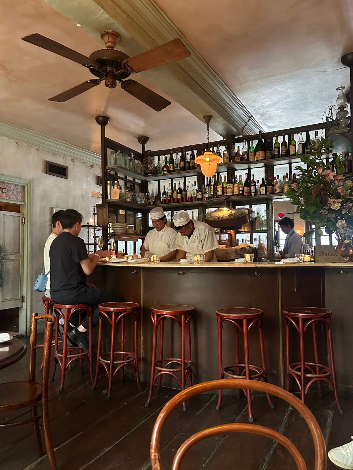 Cozy bar interior with wooden stools, shelves of bottles, and ceiling fan