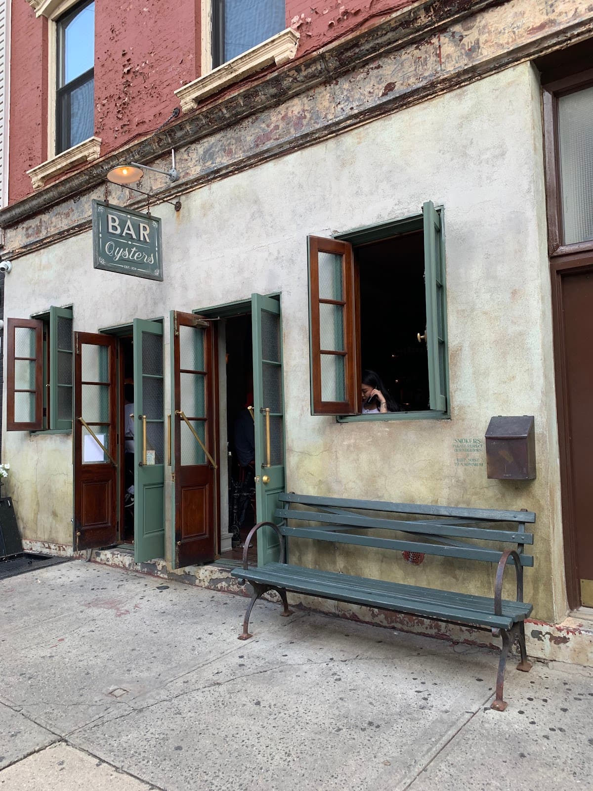 Exterior of a bar with green doors and a bench on the sidewalk in New York