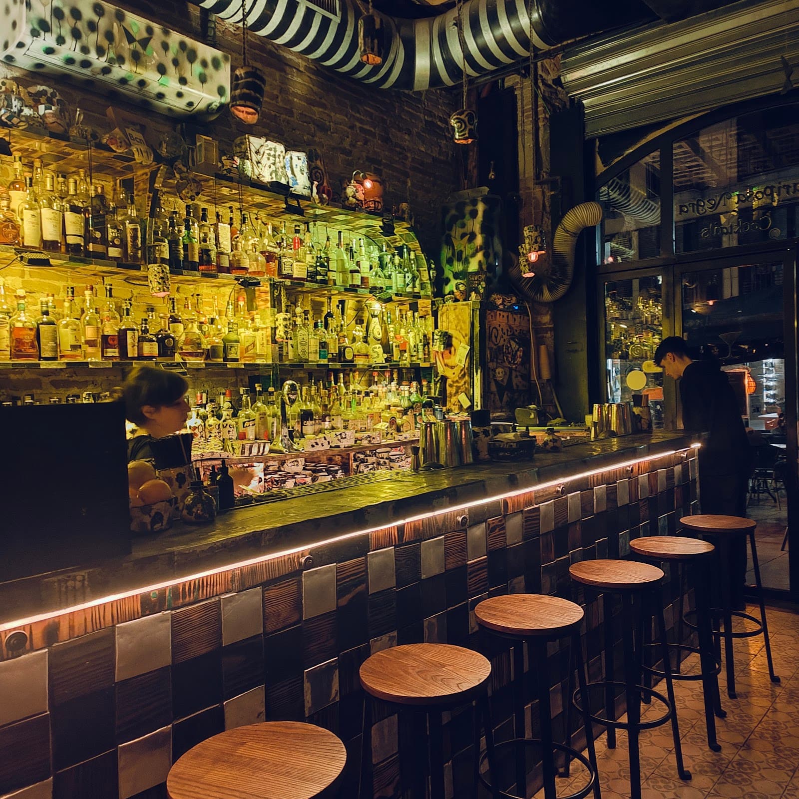 Warmly lit bar with wooden stools and a variety of bottles on shelves in Barcelona