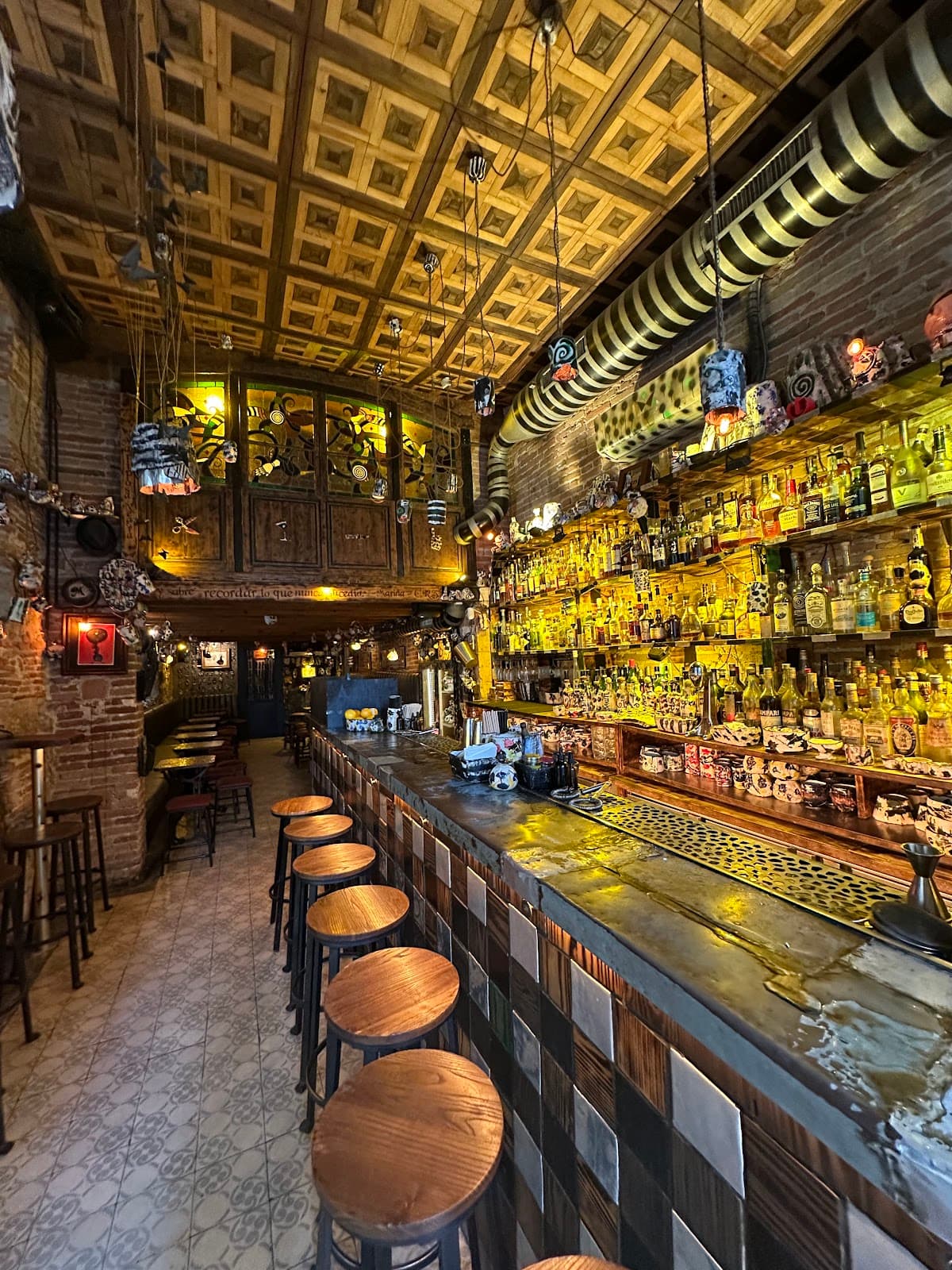 Artistic bar counter with wooden stools and decorative ceiling in Barcelona
