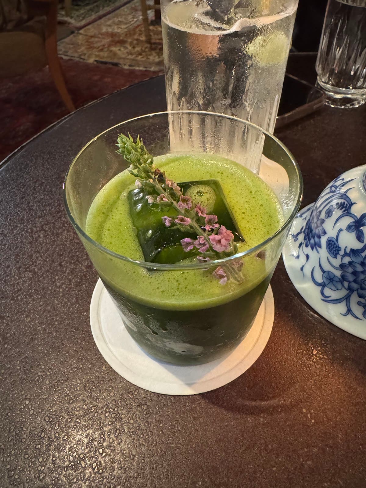 Green cocktail with floral garnish on a textured table in New York
