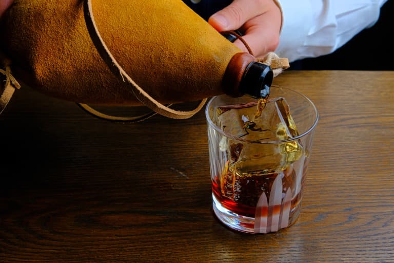 Pouring whiskey into glass with large ice cube on a wooden bar in New York