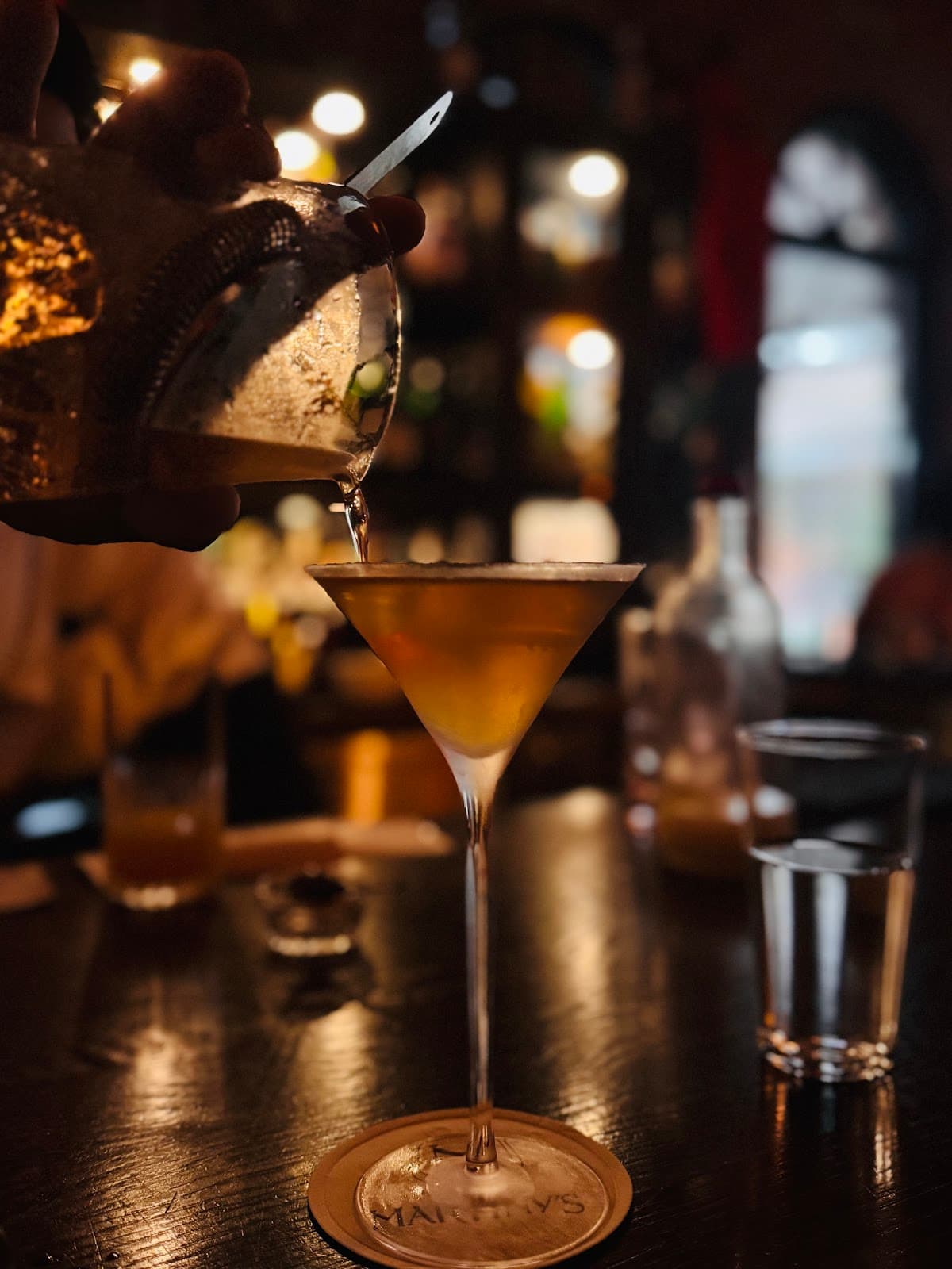 Cocktail being poured in dimly lit bar with glass on table in New York