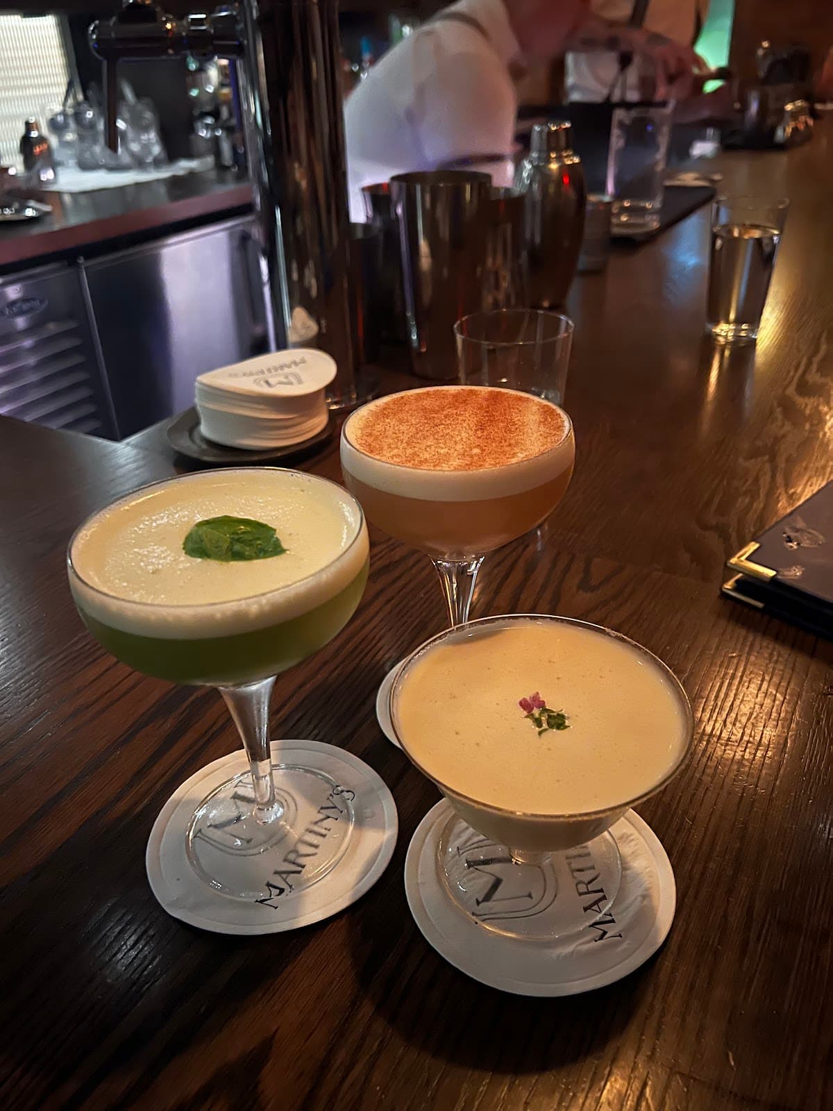 Three cocktails on a wooden bar counter with a bartender in the background. in New York