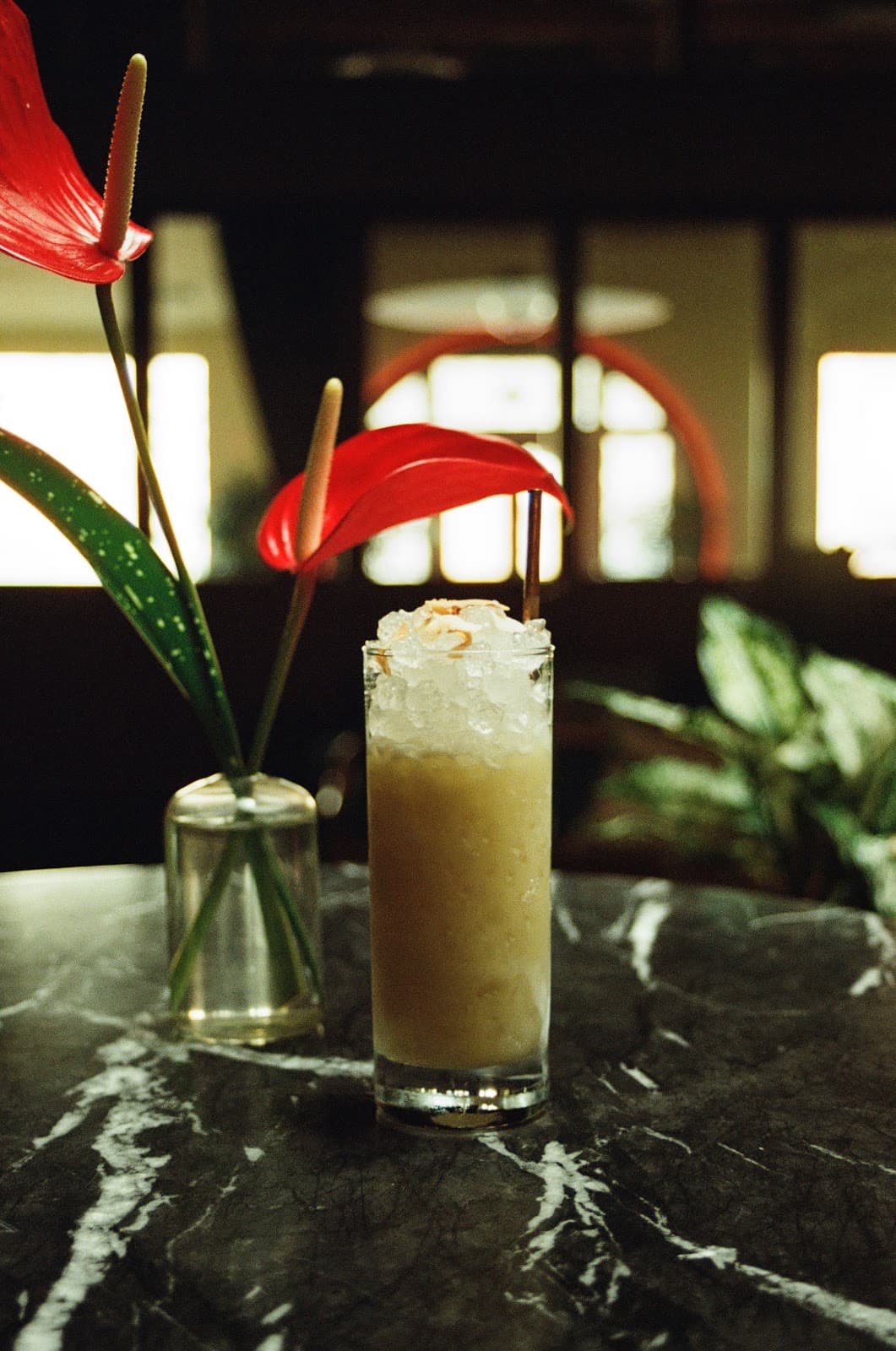 Cocktail glass with ice on a marble table near red anthurium flowers in San Francisco