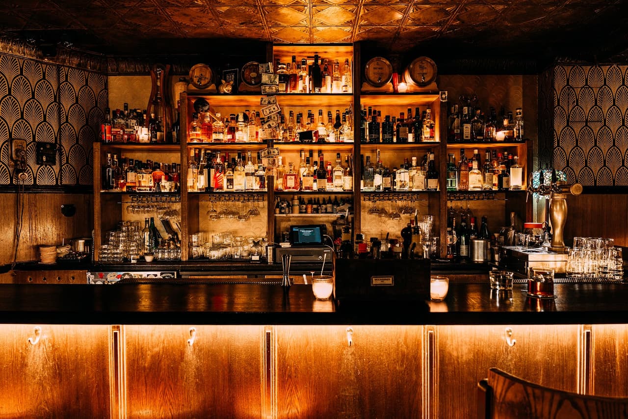 Warmly lit bar with shelves of liquor bottles and glassware