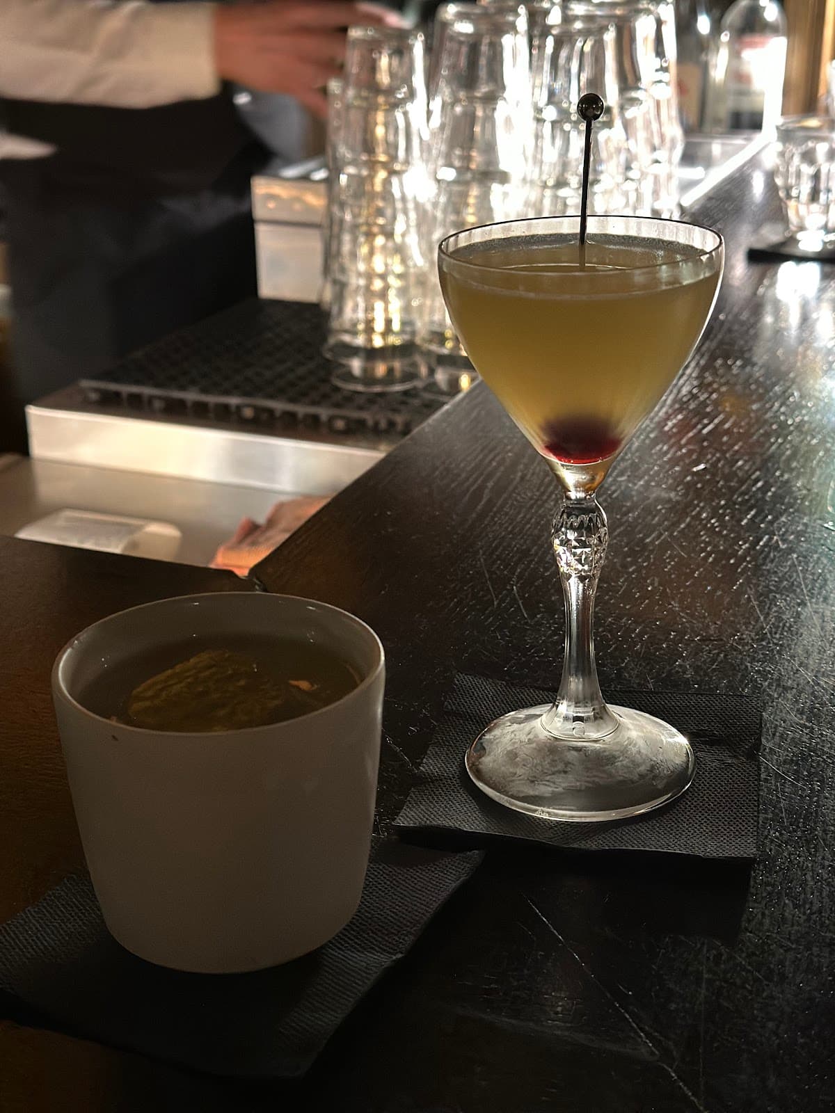 Two cocktails on a bar counter with glassware in the background in Paris