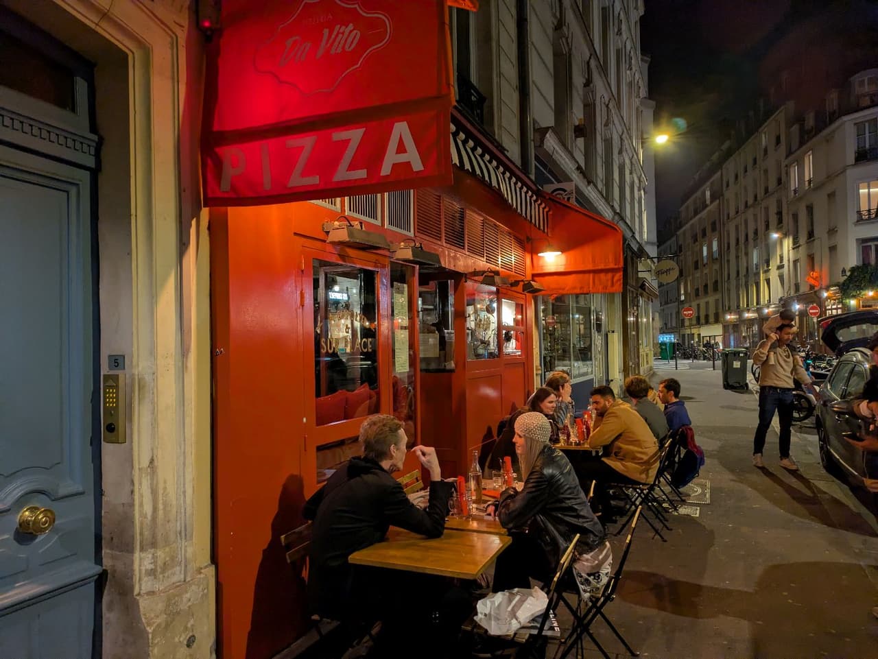 Nighttime exterior of red pizza restaurant with patrons seated outside in Paris