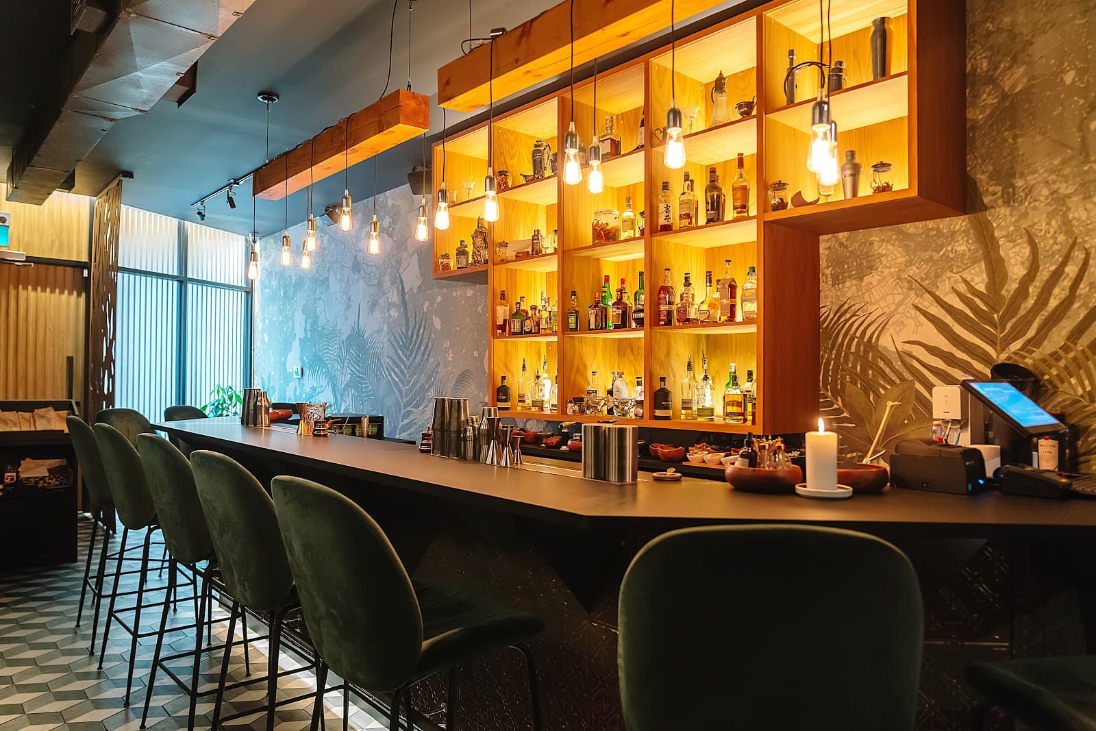 Stylish bar with green chairs, hanging lights, and filled bottle shelves