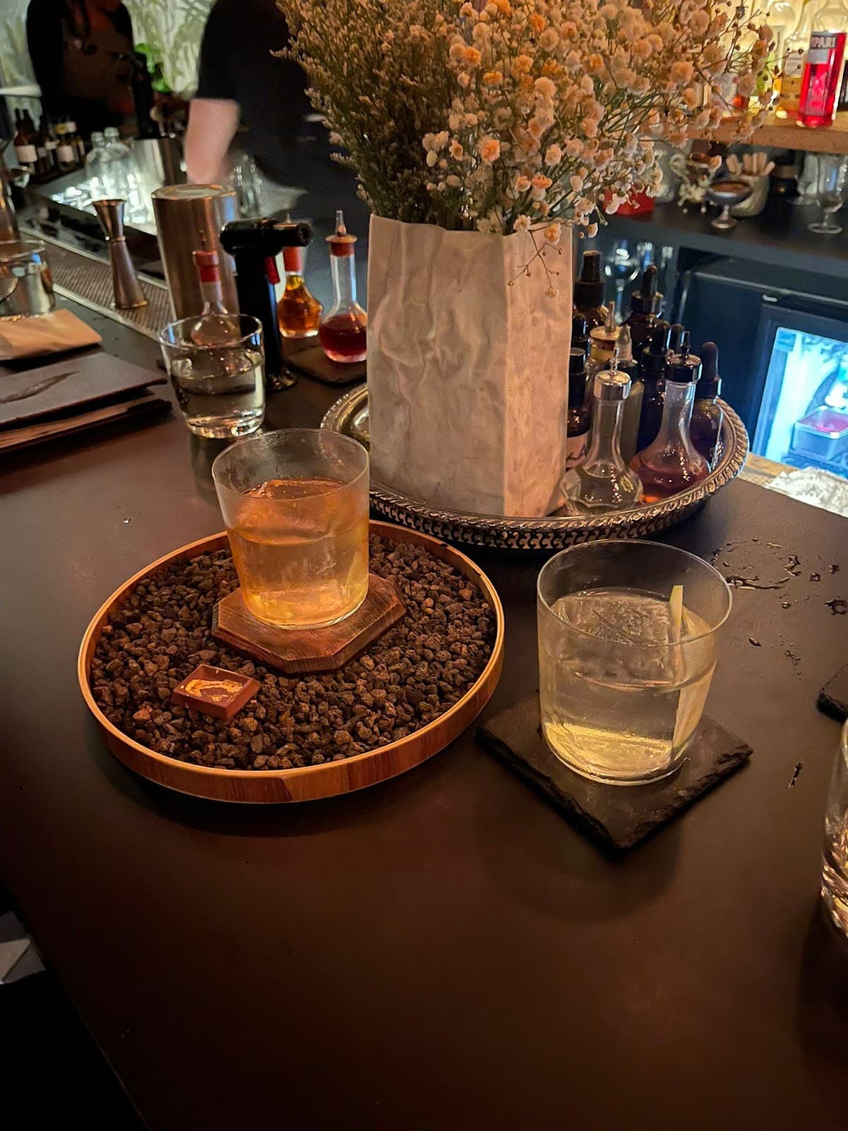 Close-up of cocktails on a bar counter with various bottles and a flower arrangement in Toronto