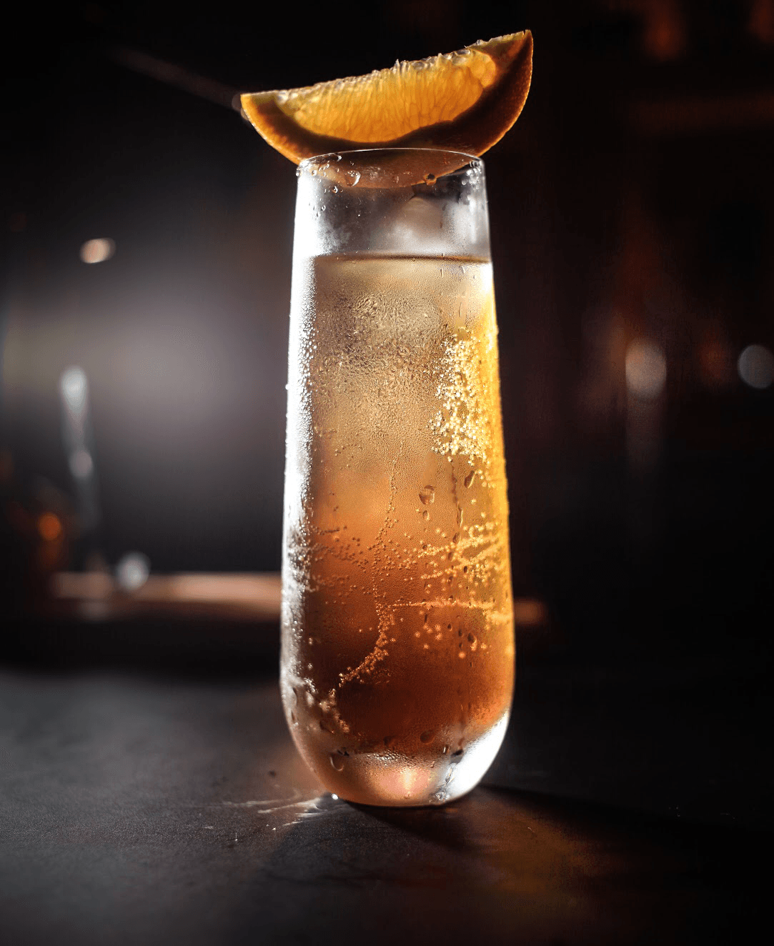 Close-up of a cocktail with an orange garnish on a dark bar setting in Toronto