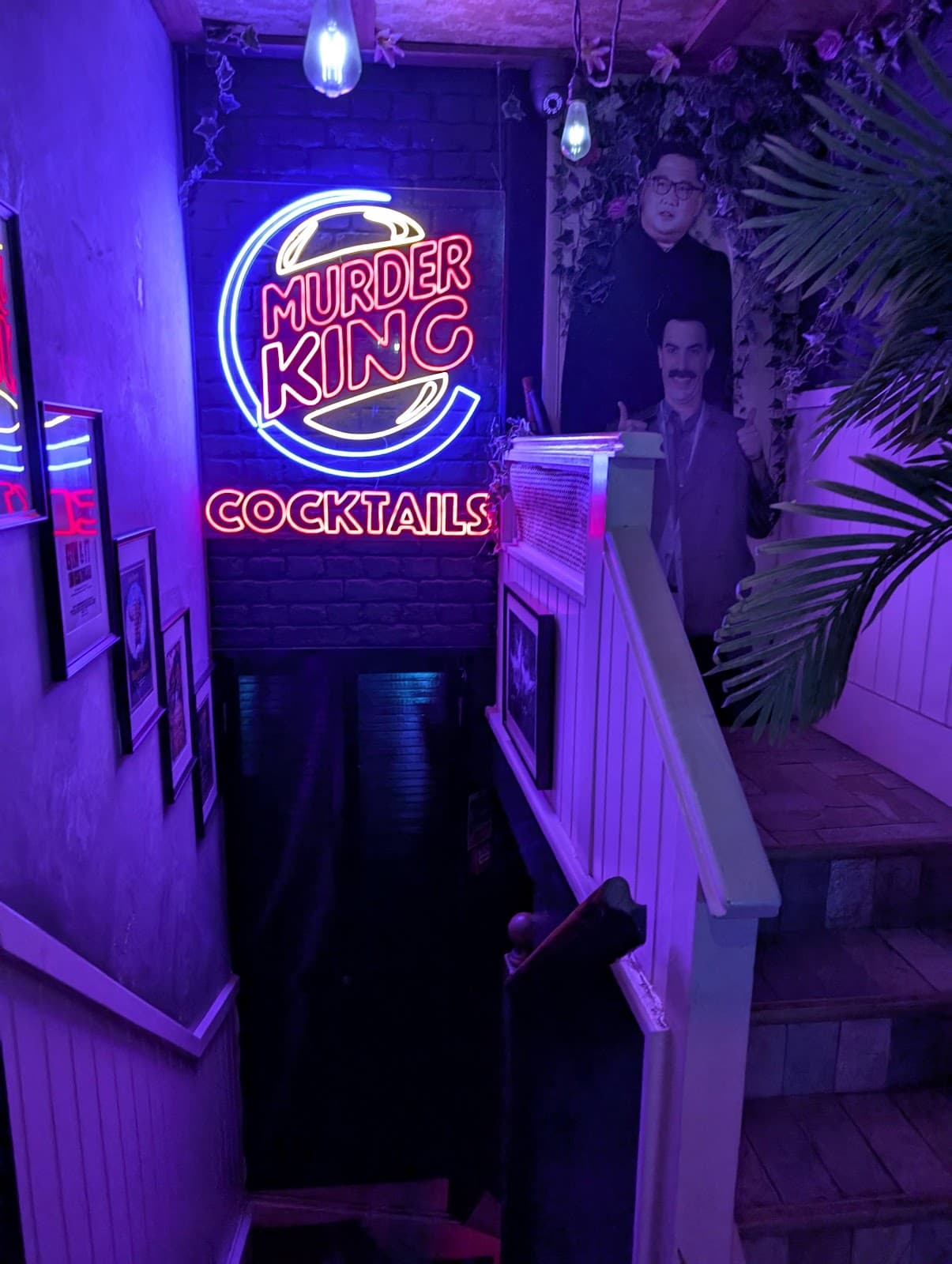 Neon sign reading 'Murder King Cocktails' in a dimly lit stairwell in London