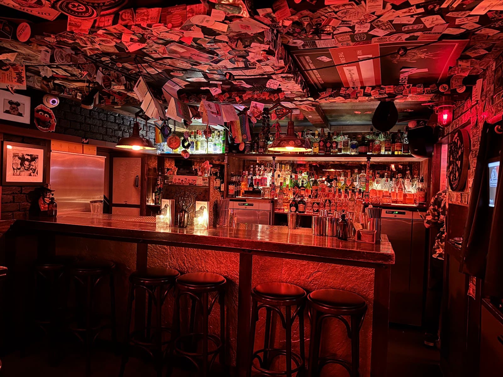Cozy bar with stools and shelves of bottles under warm red lighting in London