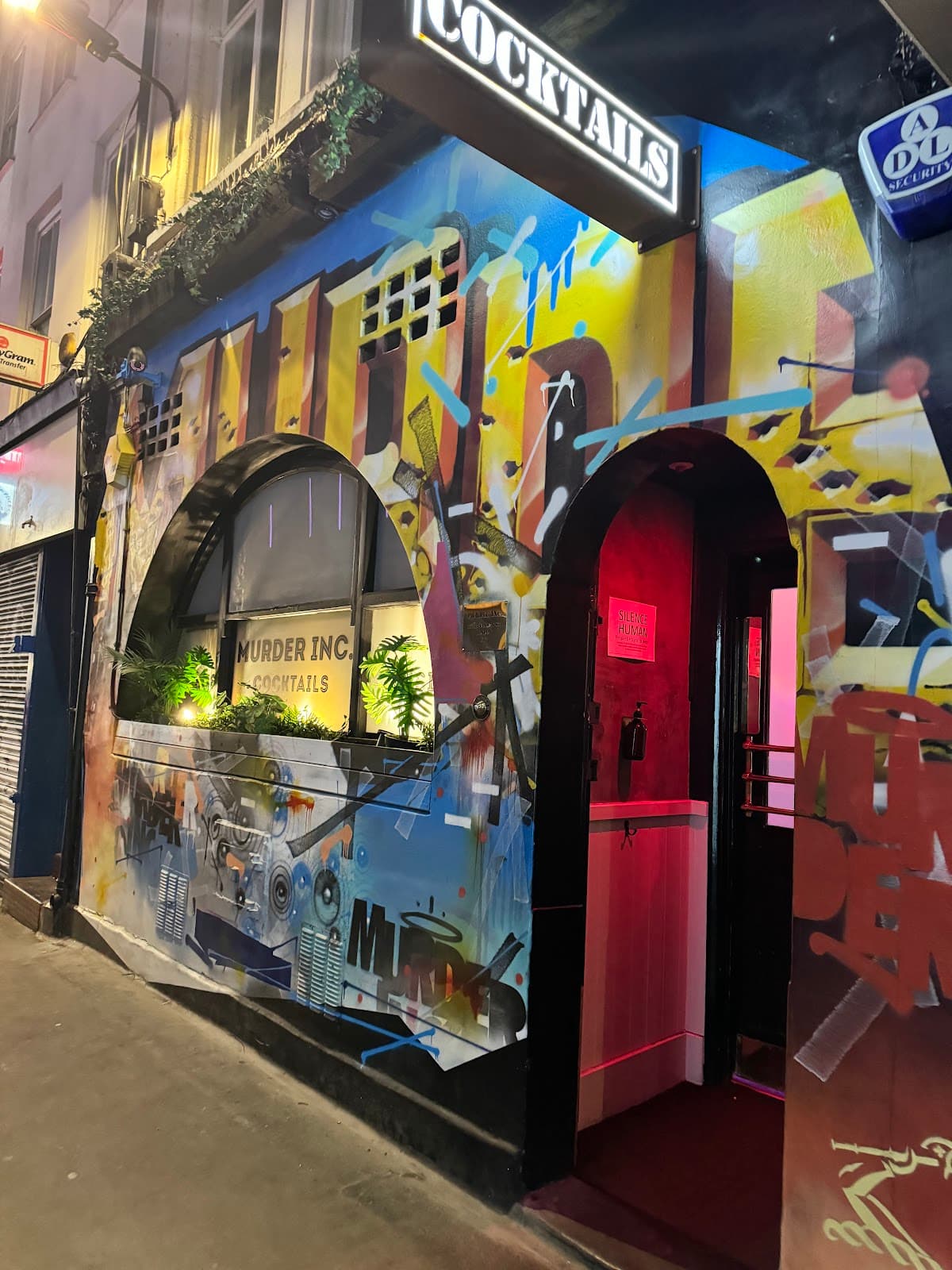 Graffiti-covered cocktail bar entrance with neon sign in London