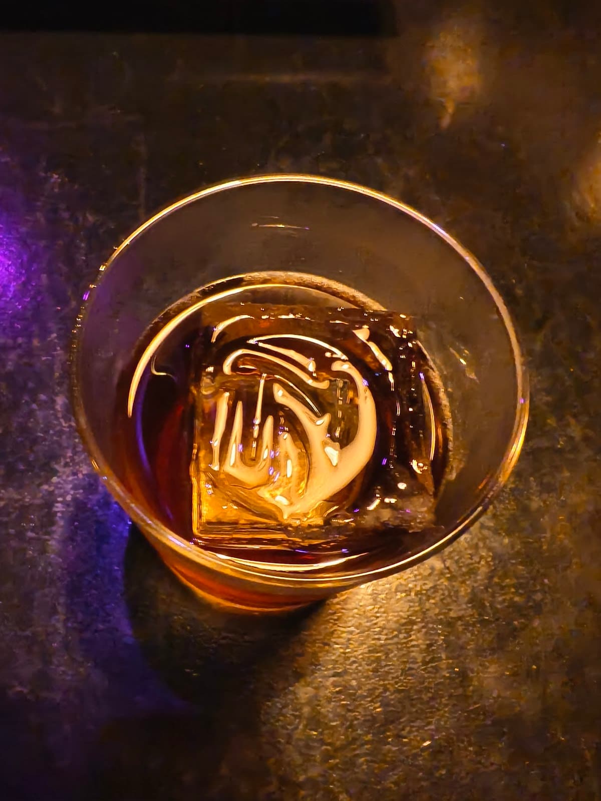 Close-up of a cocktail with a large ice cube on a dimly lit table in Edinburgh