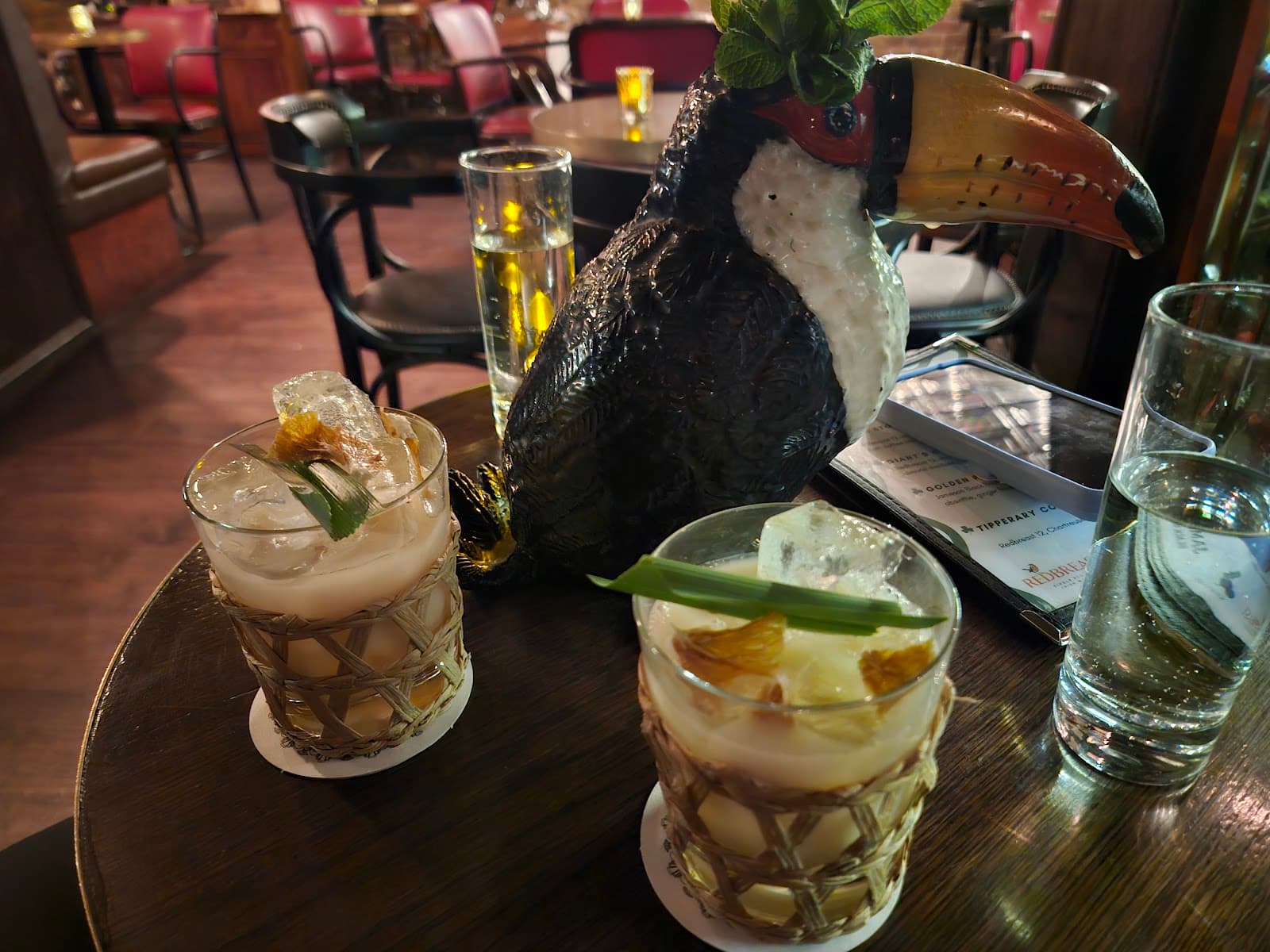 Cocktails on a wooden table with a toucan figurine in a dimly lit bar in London