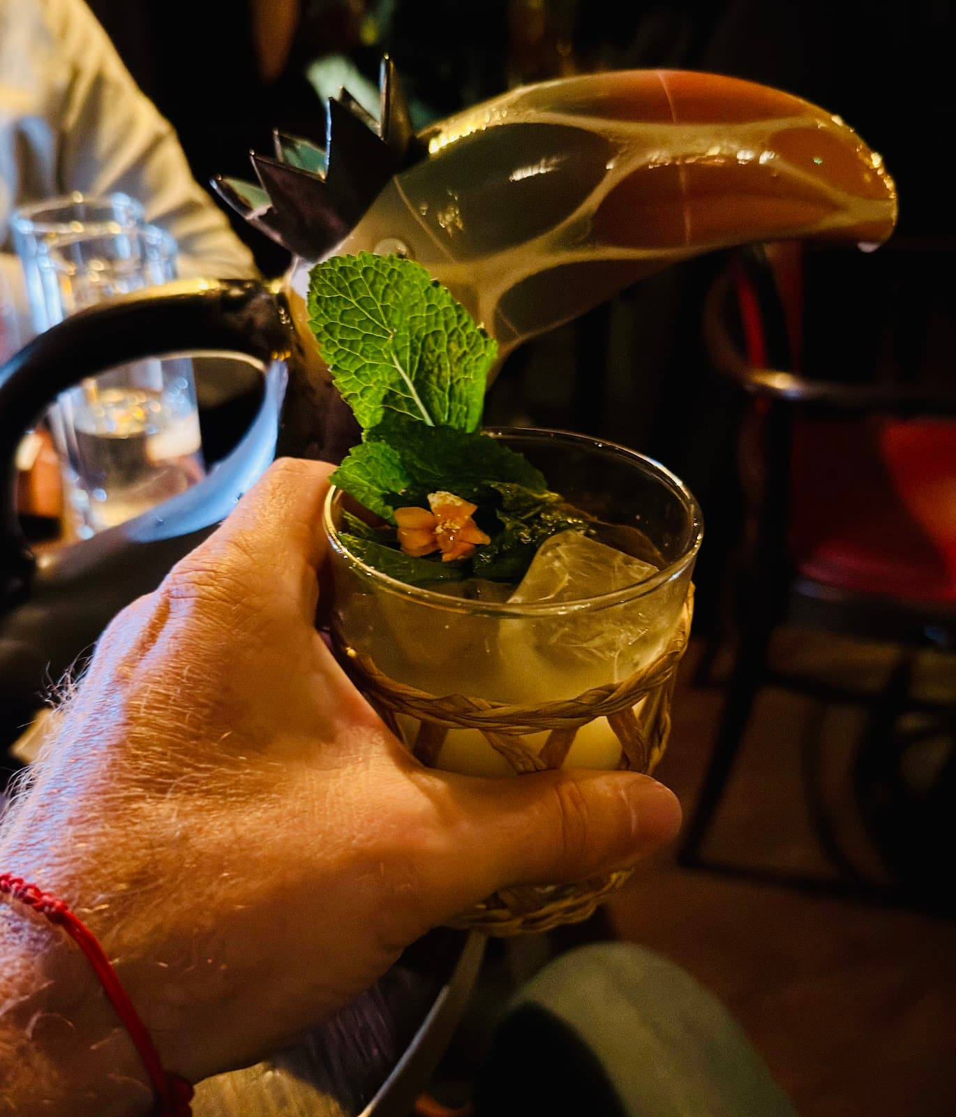 Close-up of a cocktail with mint leaves held by a person in a dimly lit bar in London