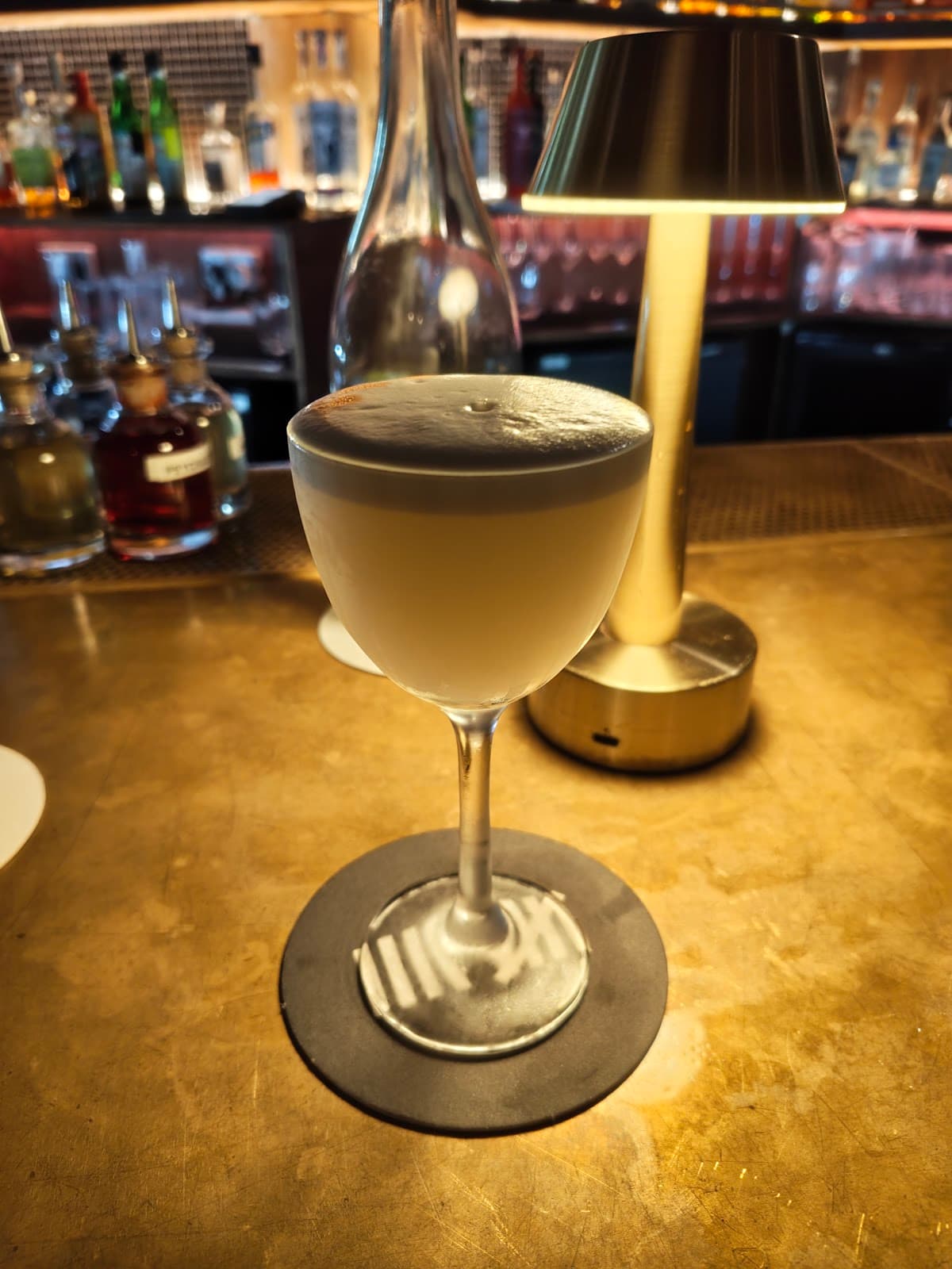 Close-up of a cocktail on a bar counter with a lamp in the background in London
