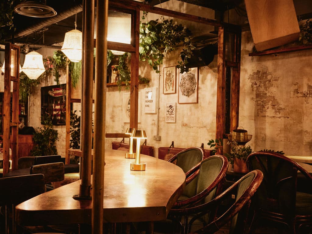 Cozy bar interior with warm lighting, plants, and art on the walls.