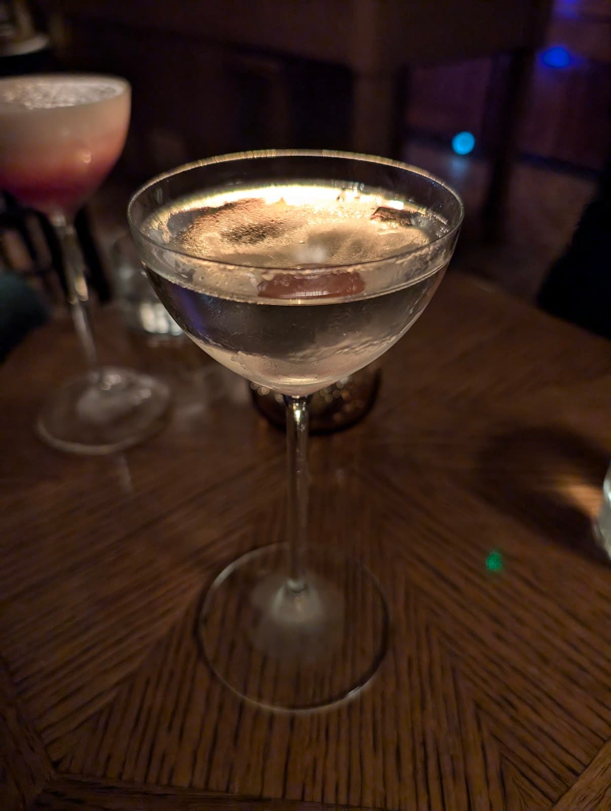 Cocktail glass with an olive set on a wooden table in a dimly lit bar in London