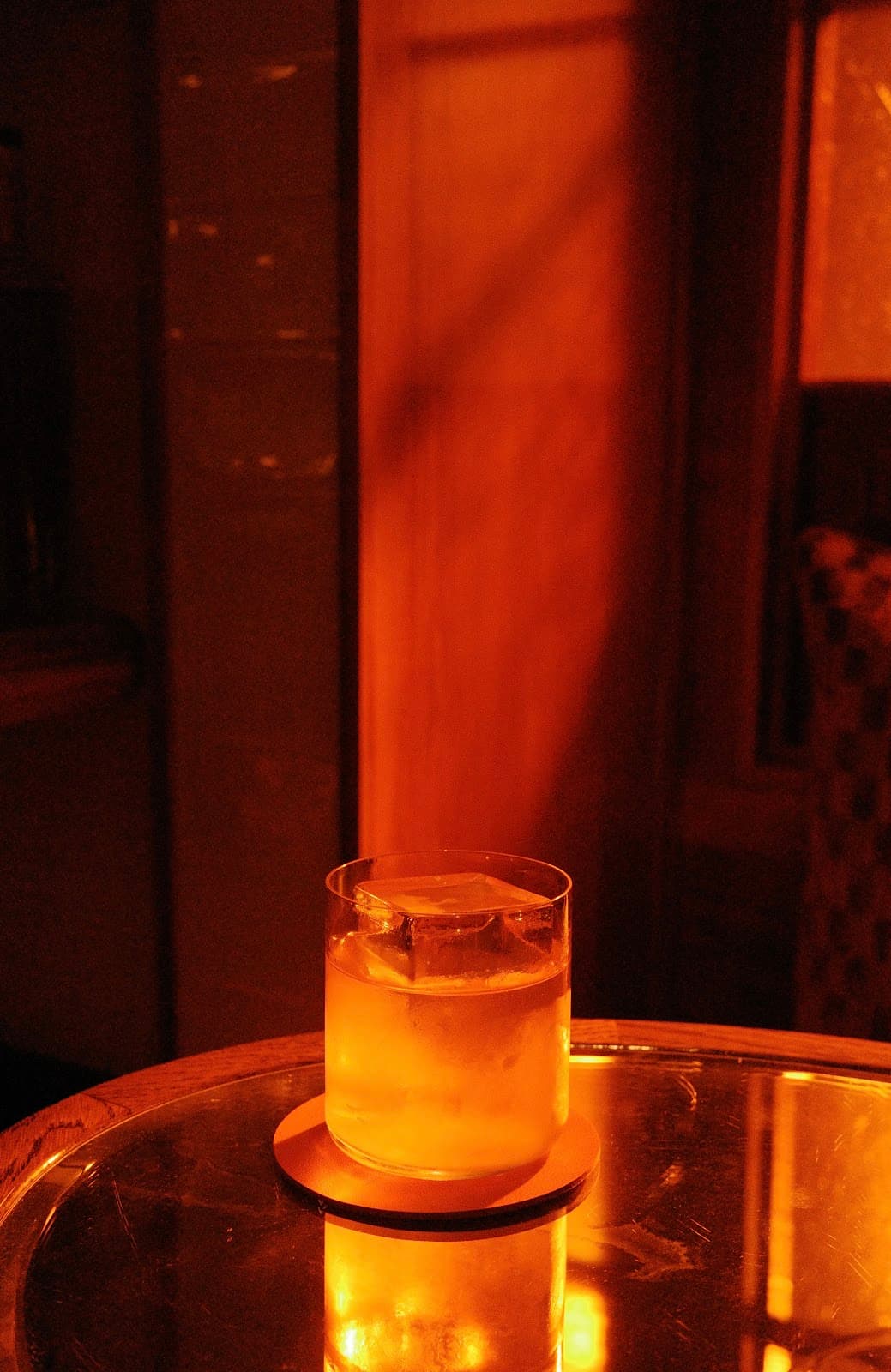 Low-lit cocktail with ice on a reflective table in warm orange ambiance in London