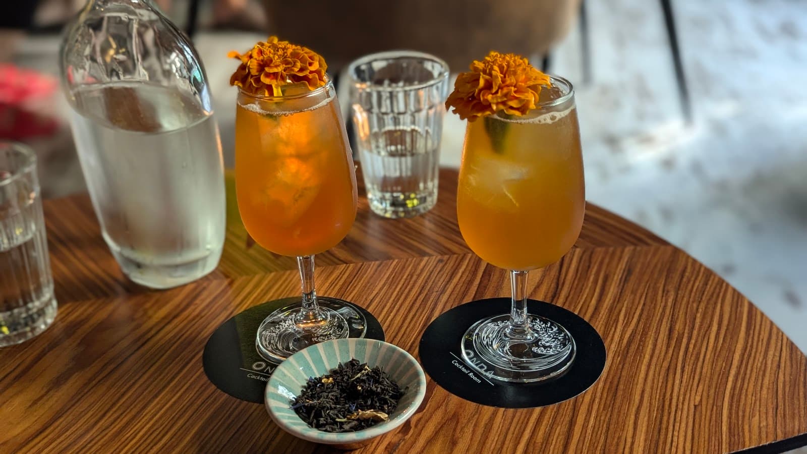Two cocktails with orange flowers on a table with a glass bottle in Lisboa