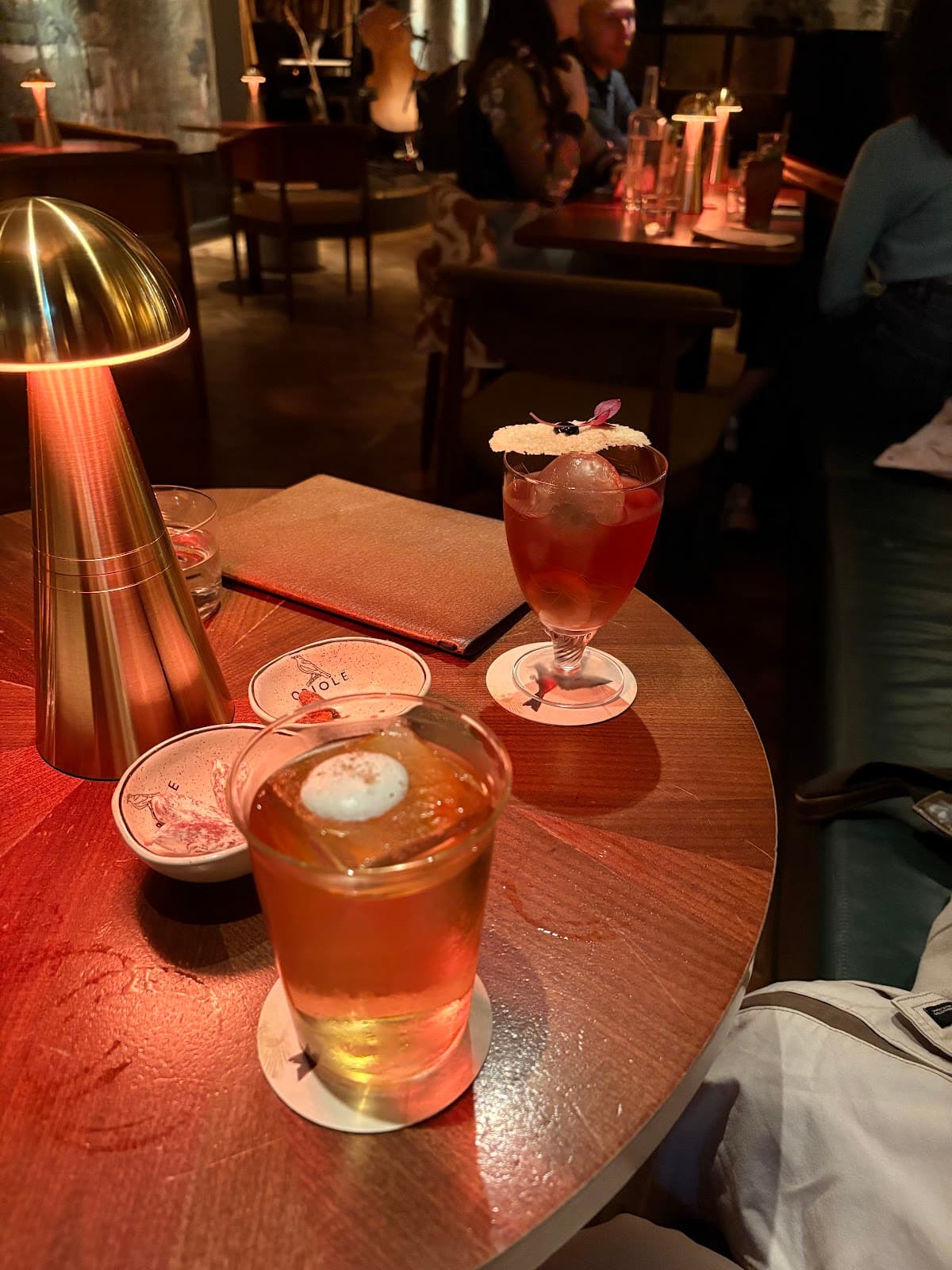 Close-up of two cocktails on a wooden table with a warm lamp in London
