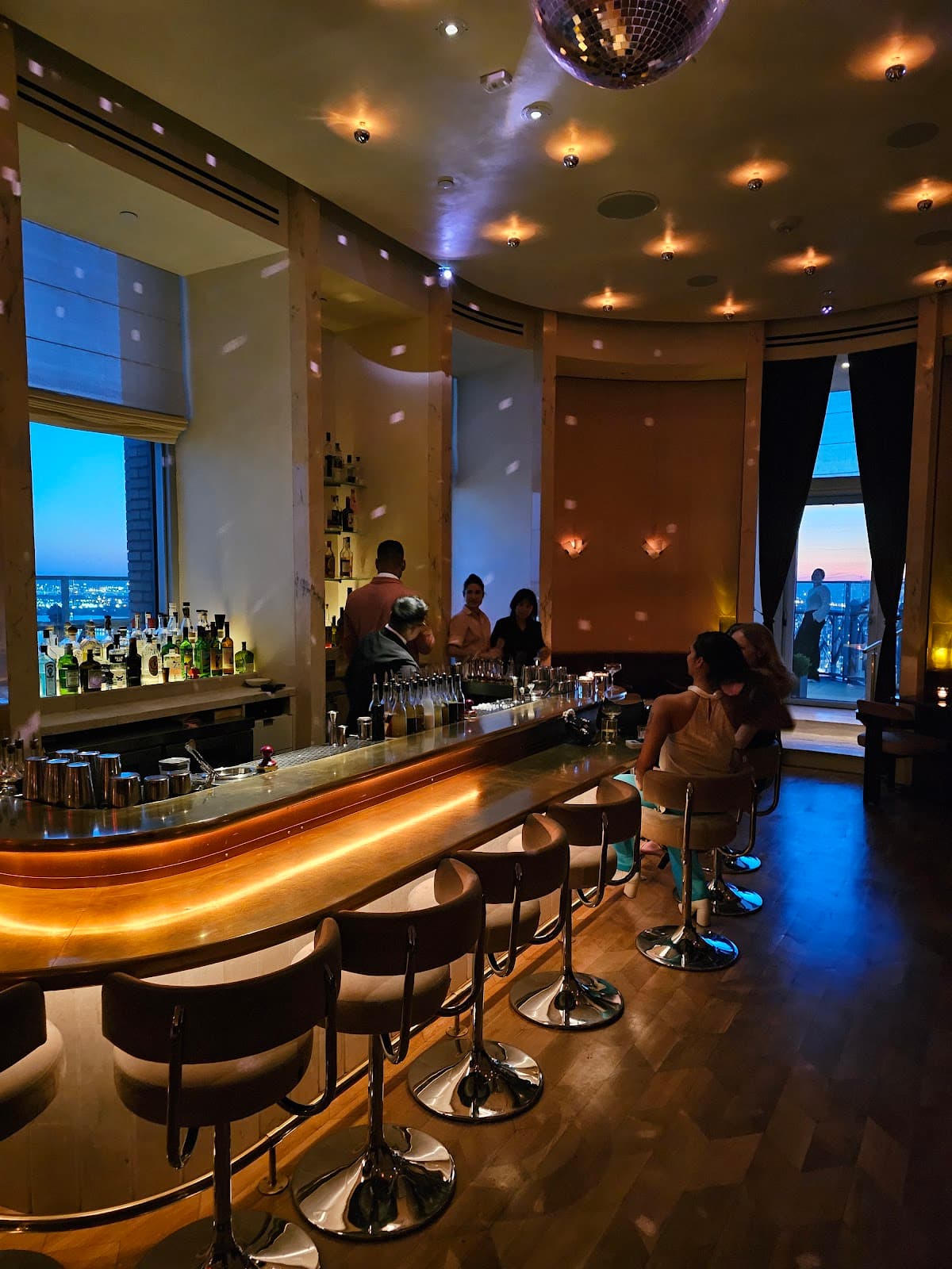 Stylish bar interior with illuminated counter and city view at dusk