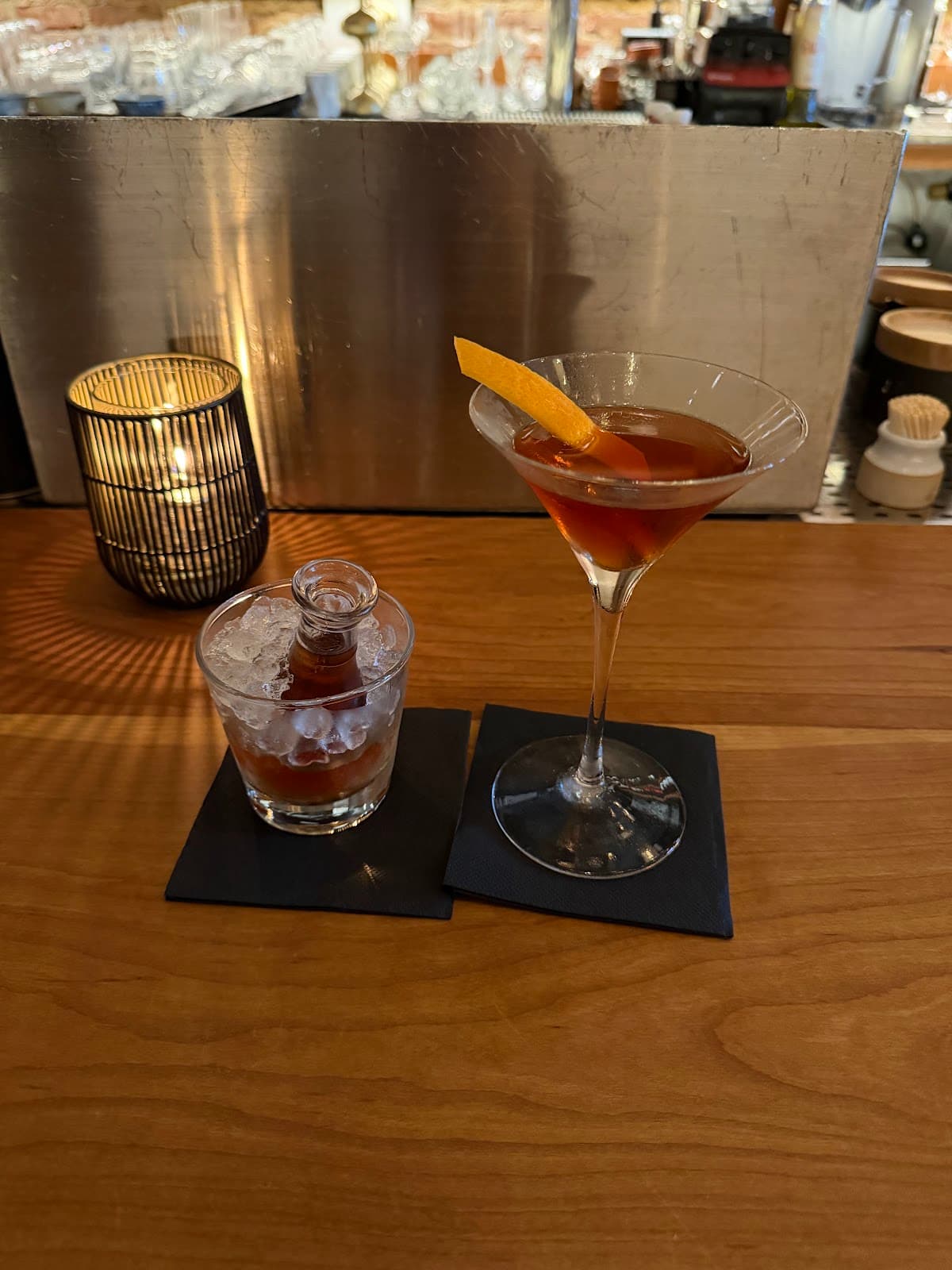 Two cocktails on a bar top with a small candle and metal background in San Francisco
